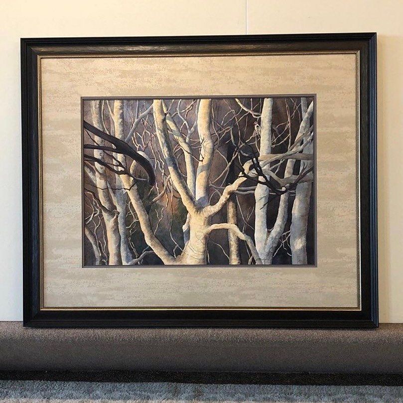 Framed painting of bare trees in a forest. Light highlights white bark against dark branches and background.