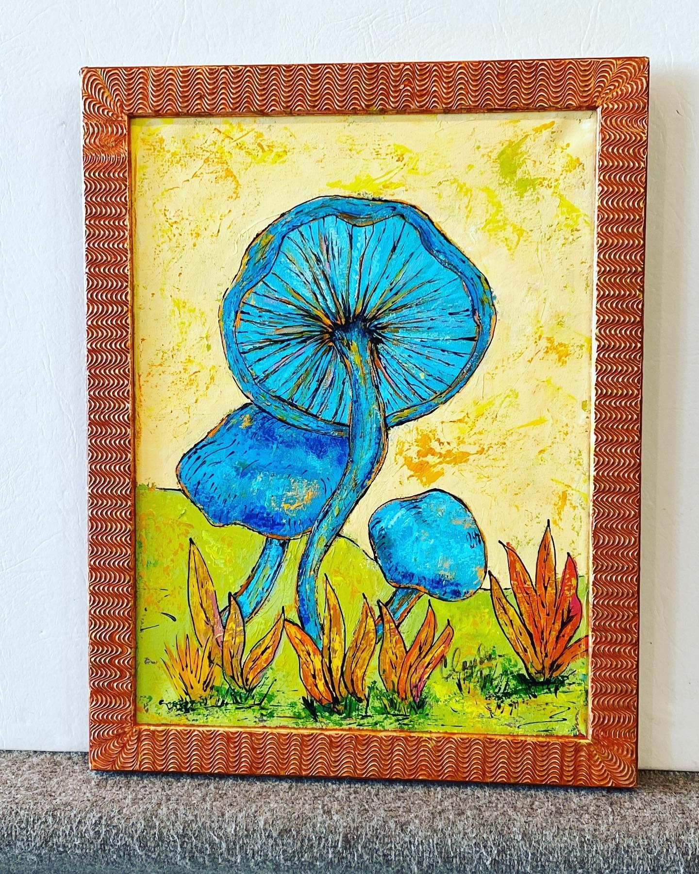 Blue mushrooms in a grassy field, painted on a textured canvas in an orange frame.