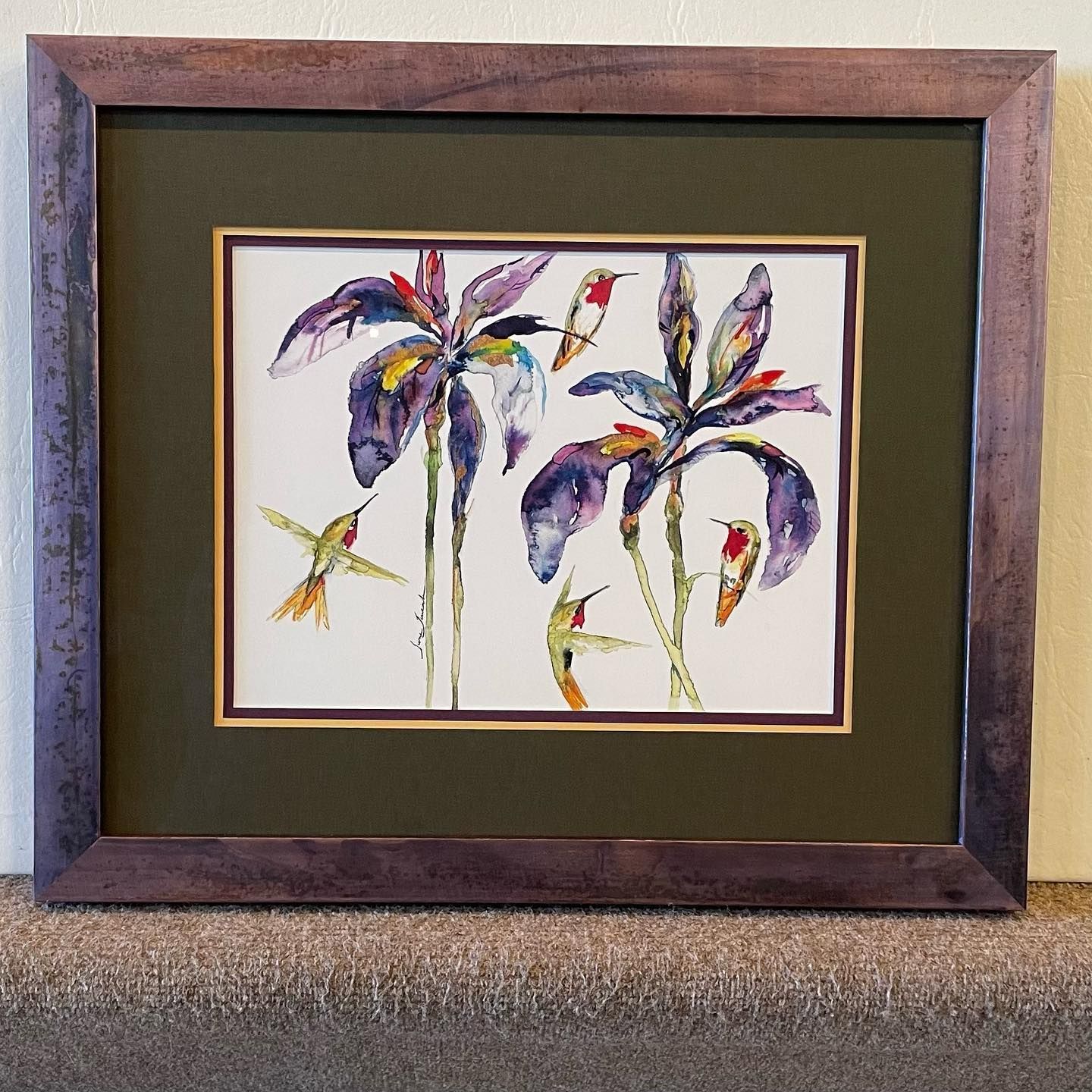 Watercolor of hummingbirds and purple irises in a framed display; green matte, brown frame.