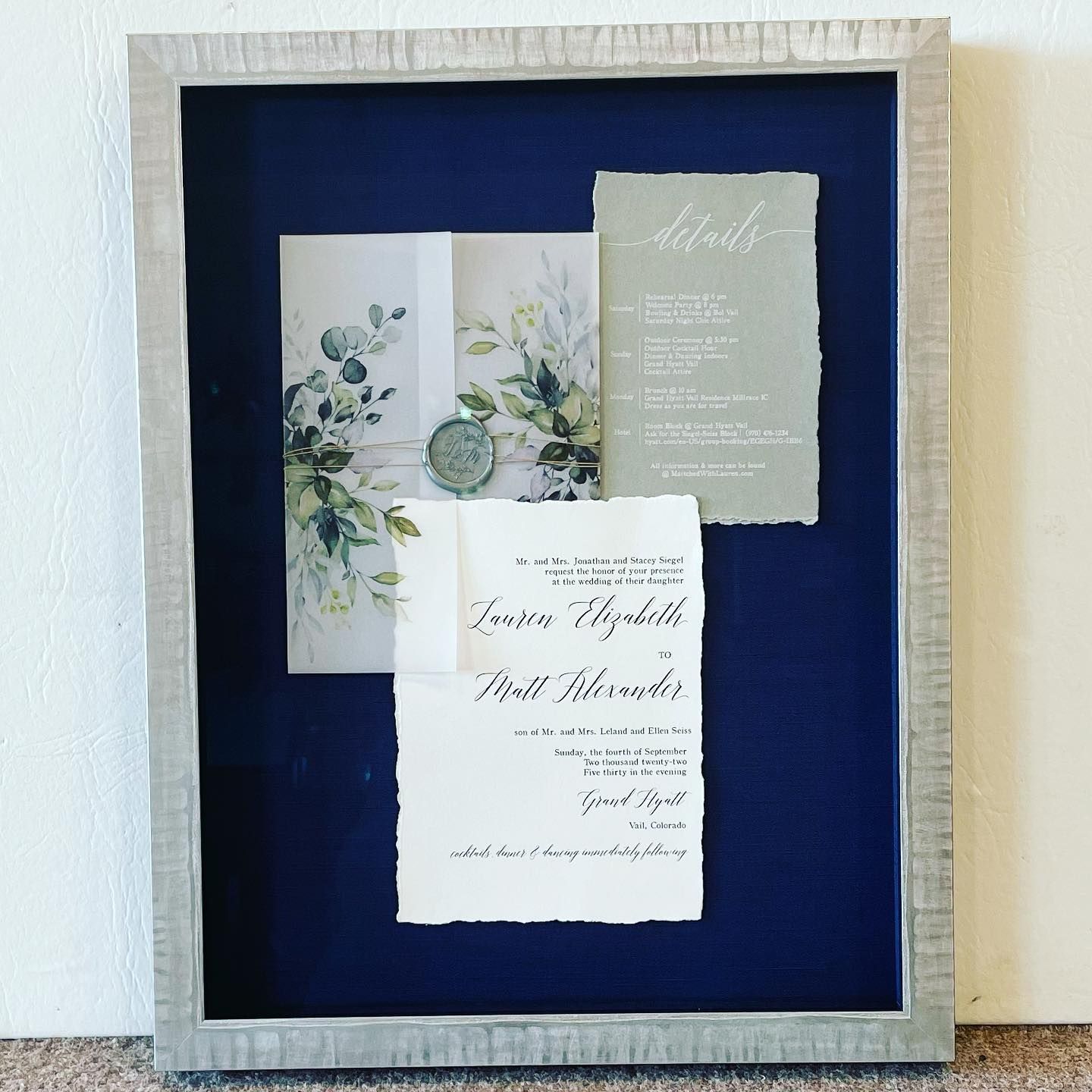 Framed wedding invitations with navy background. Includes floral details, calligraphy, and wax seal.