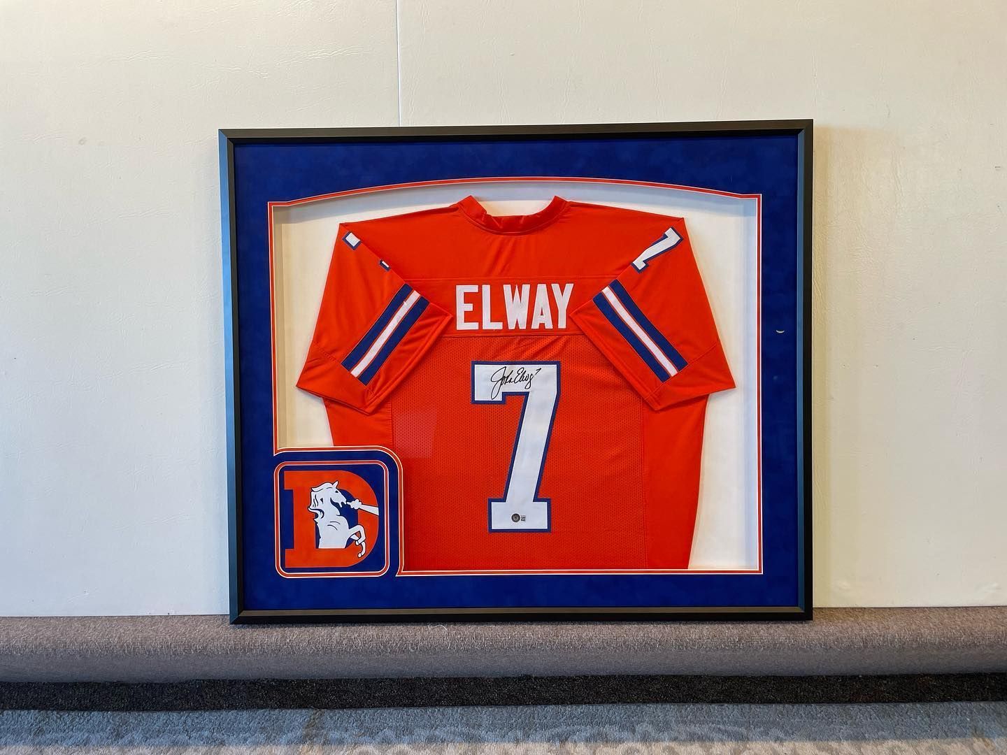 Framed John Elway Broncos jersey with signature, orange, blue, and white.