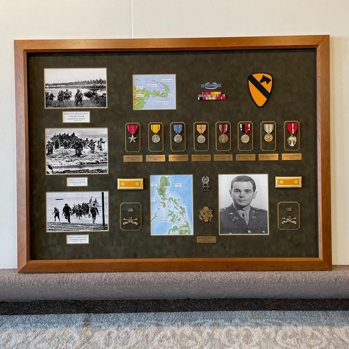 Military display case with photos, medals, patches, and a portrait of a serviceman.