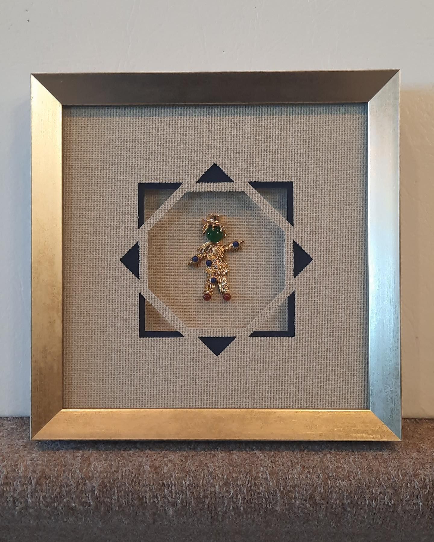 Framed artwork: gingerbread man charm inside a geometric shape, on a textured neutral background.