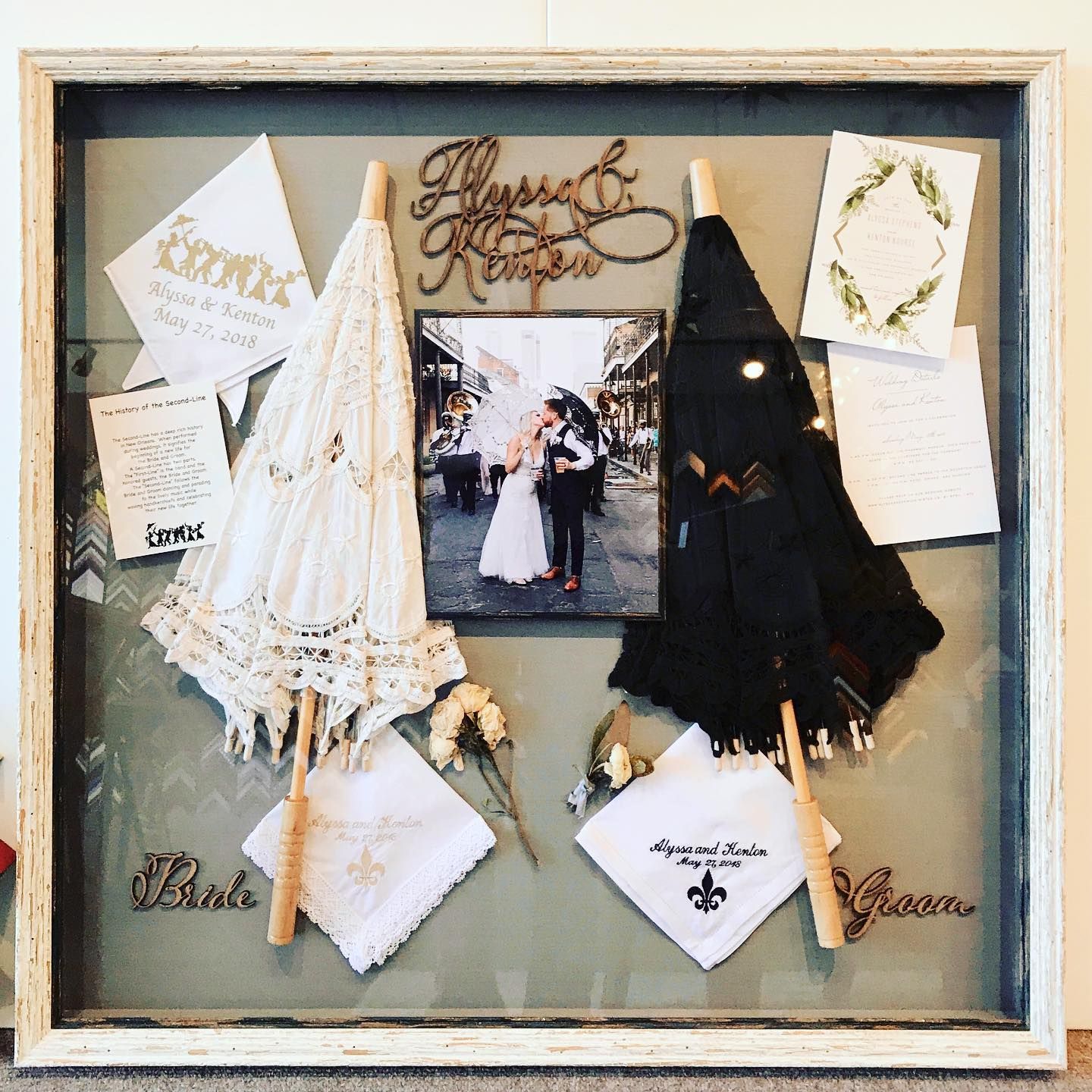 Shadow box with wedding mementos: photo, parasols, handkerchiefs. Rustic wood frame, light and dark colors.