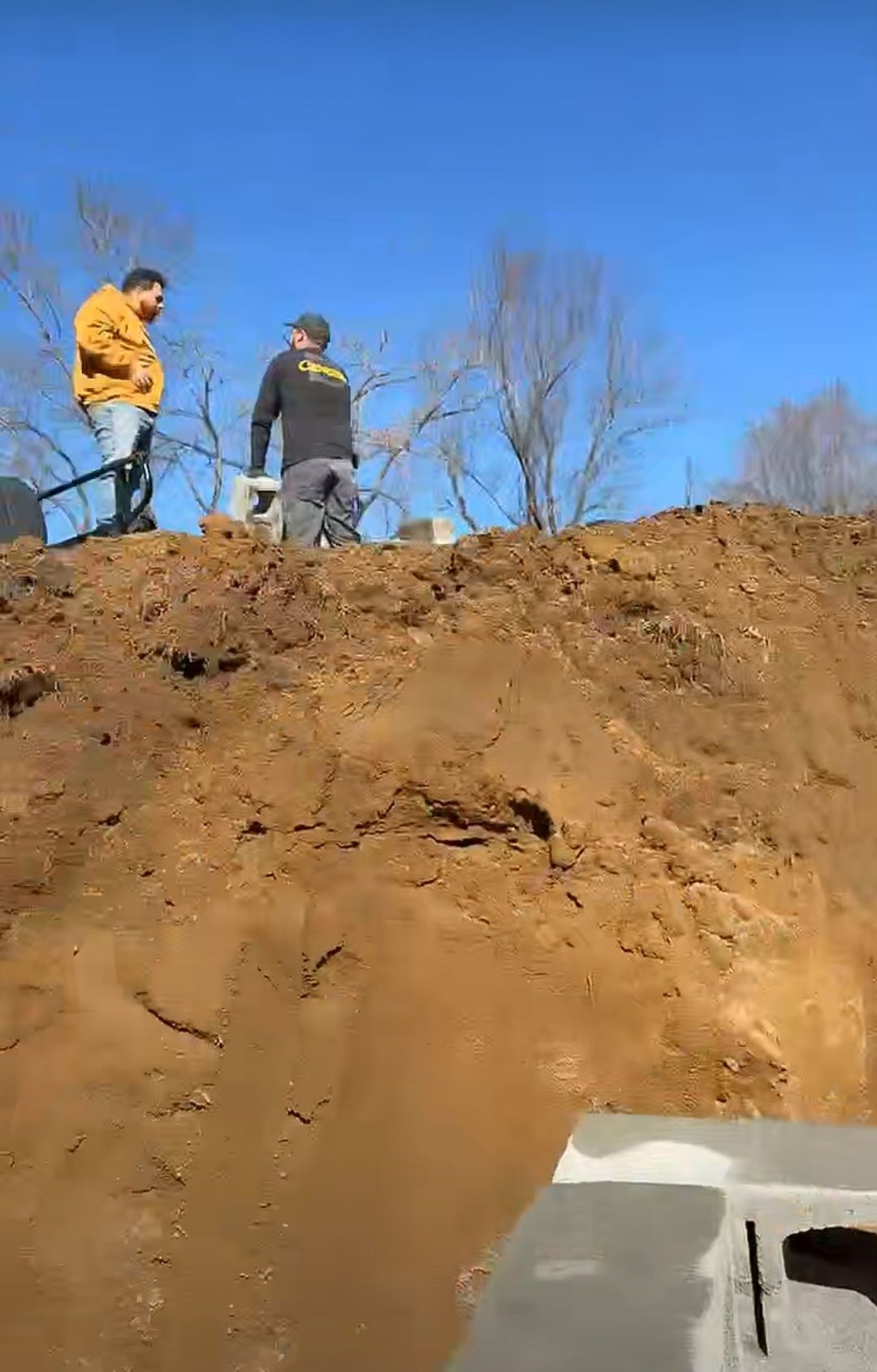 Two men are standing on top of a pile of dirt.