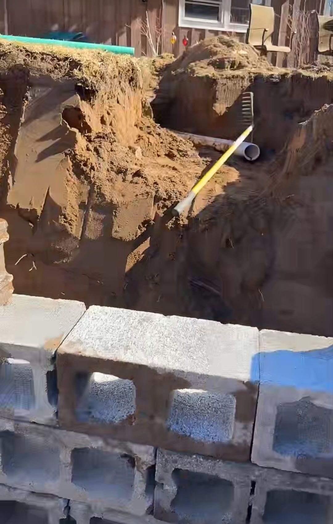 A large hole in the ground is being filled with dirt and concrete blocks.