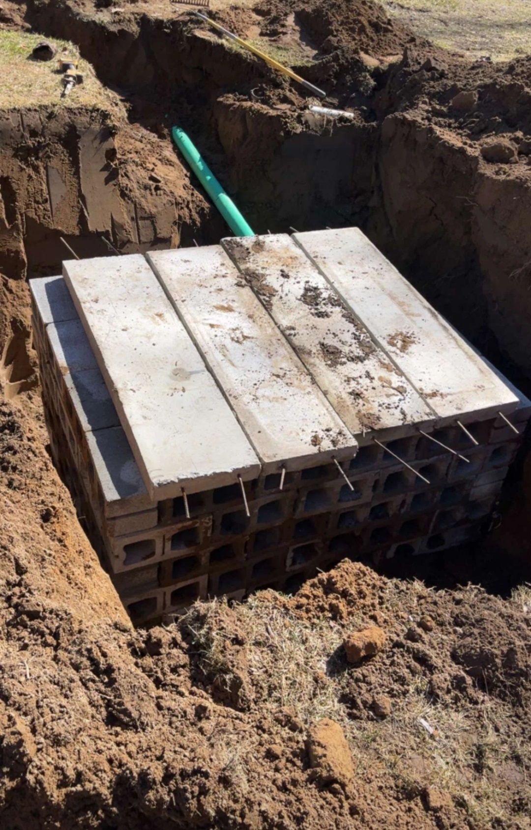 A concrete block is sitting in the dirt next to a pipe.
