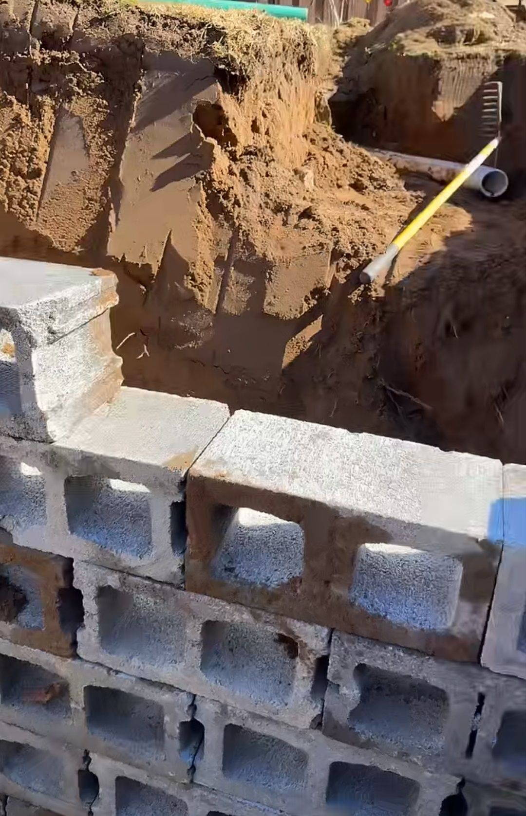 A brick wall is being built next to a hole in the ground.