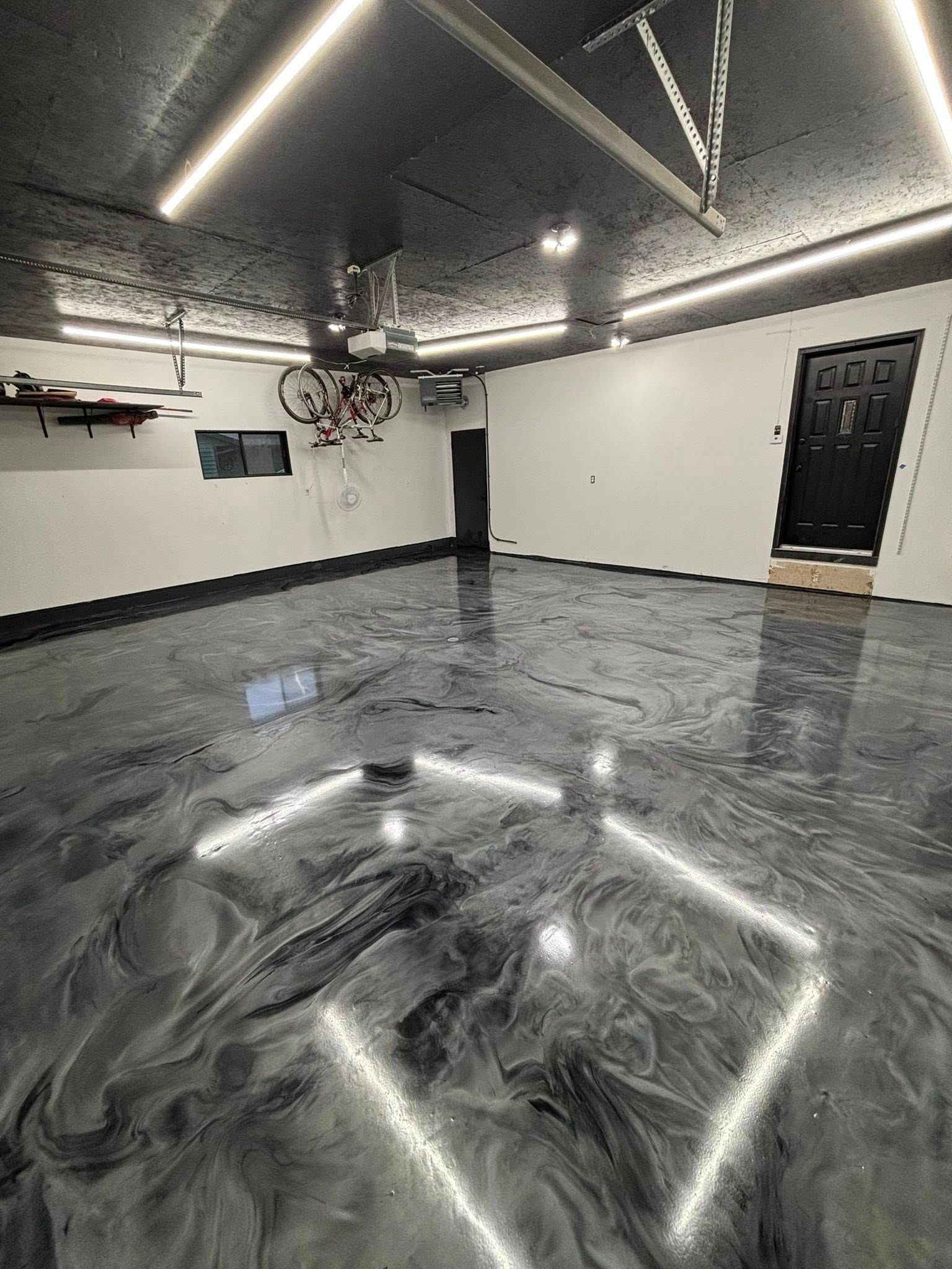 Empty garage with glossy black floor, white walls, overhead lights, and a black door.