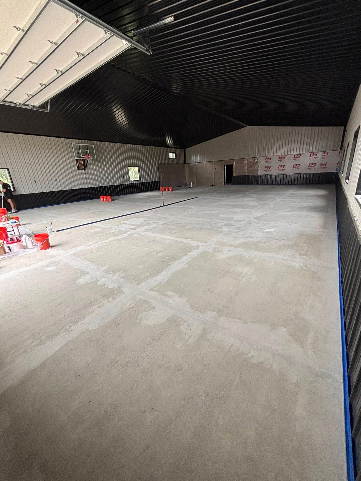 Empty indoor parking garage with a concrete floor, black ceiling, and red traffic cones along the left side.