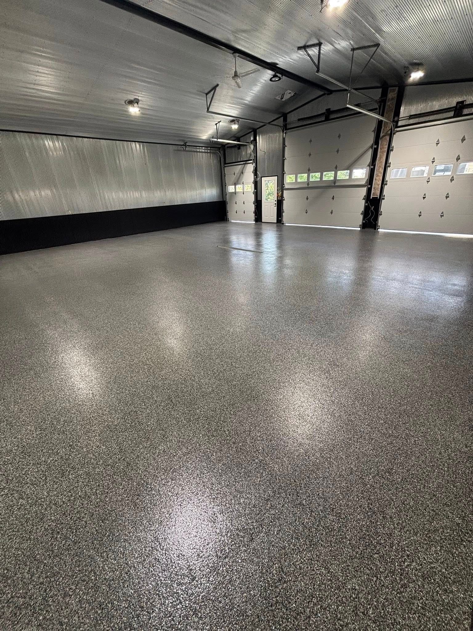 Empty indoor hall with speckled epoxy floor and dark insulated ceiling under bright lights
