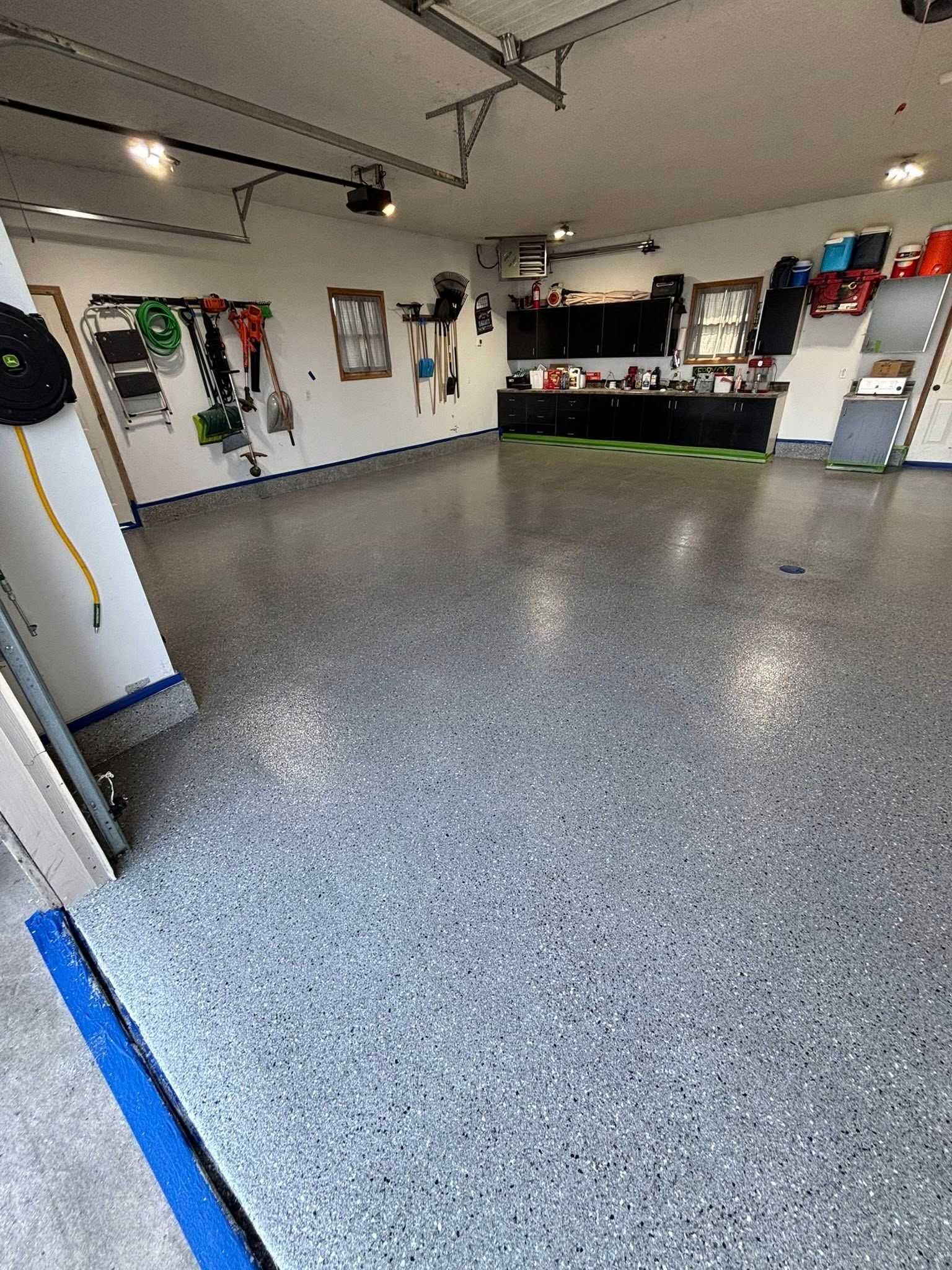 Empty garage with speckled epoxy floor, wall-mounted tools, and a workbench along the back wall.