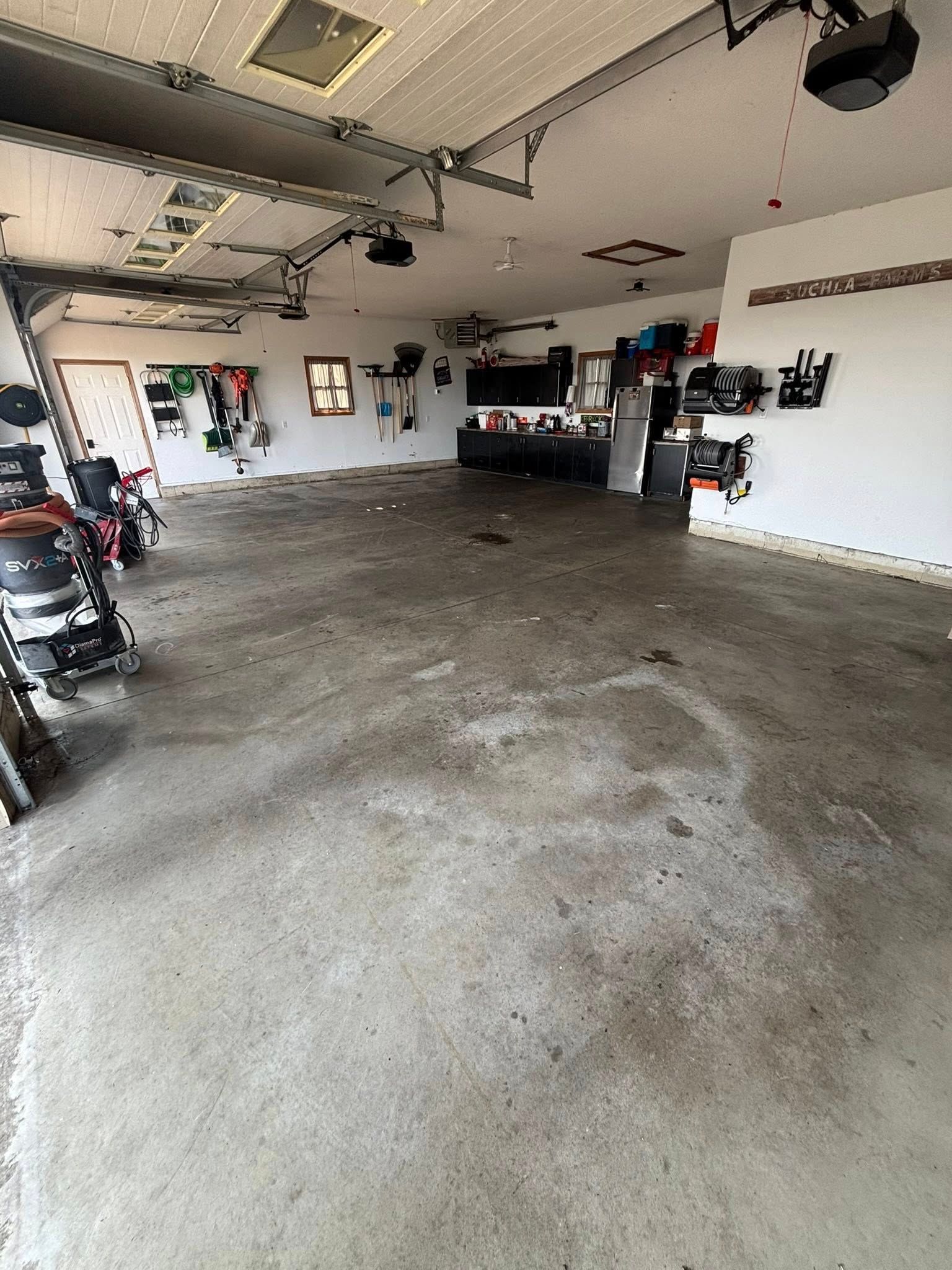 Empty garage with concrete floor, white walls, overhead storage, and a motorcycle at left.