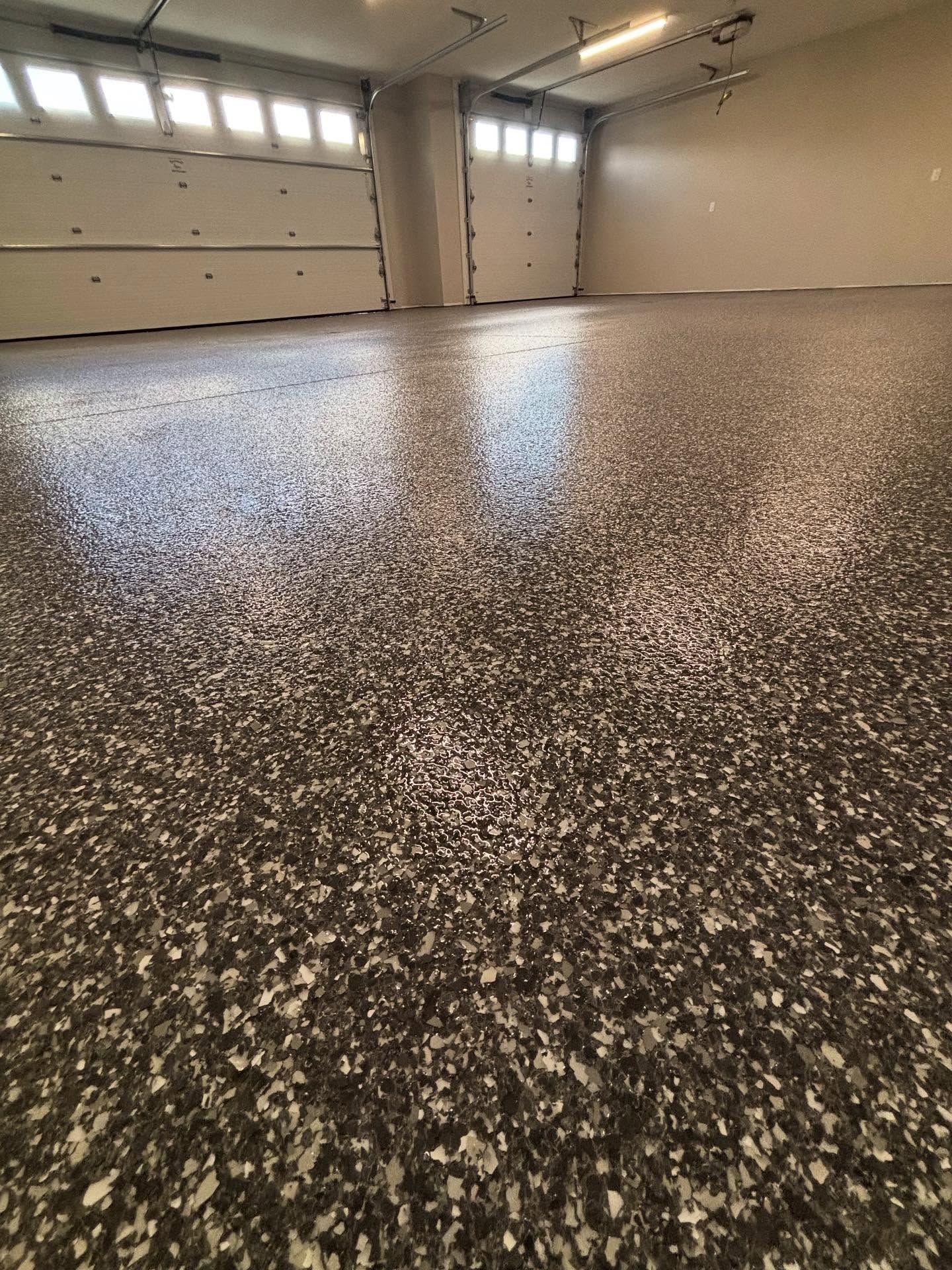 Empty garage with speckled epoxy floor and closed beige doors under ceiling lights