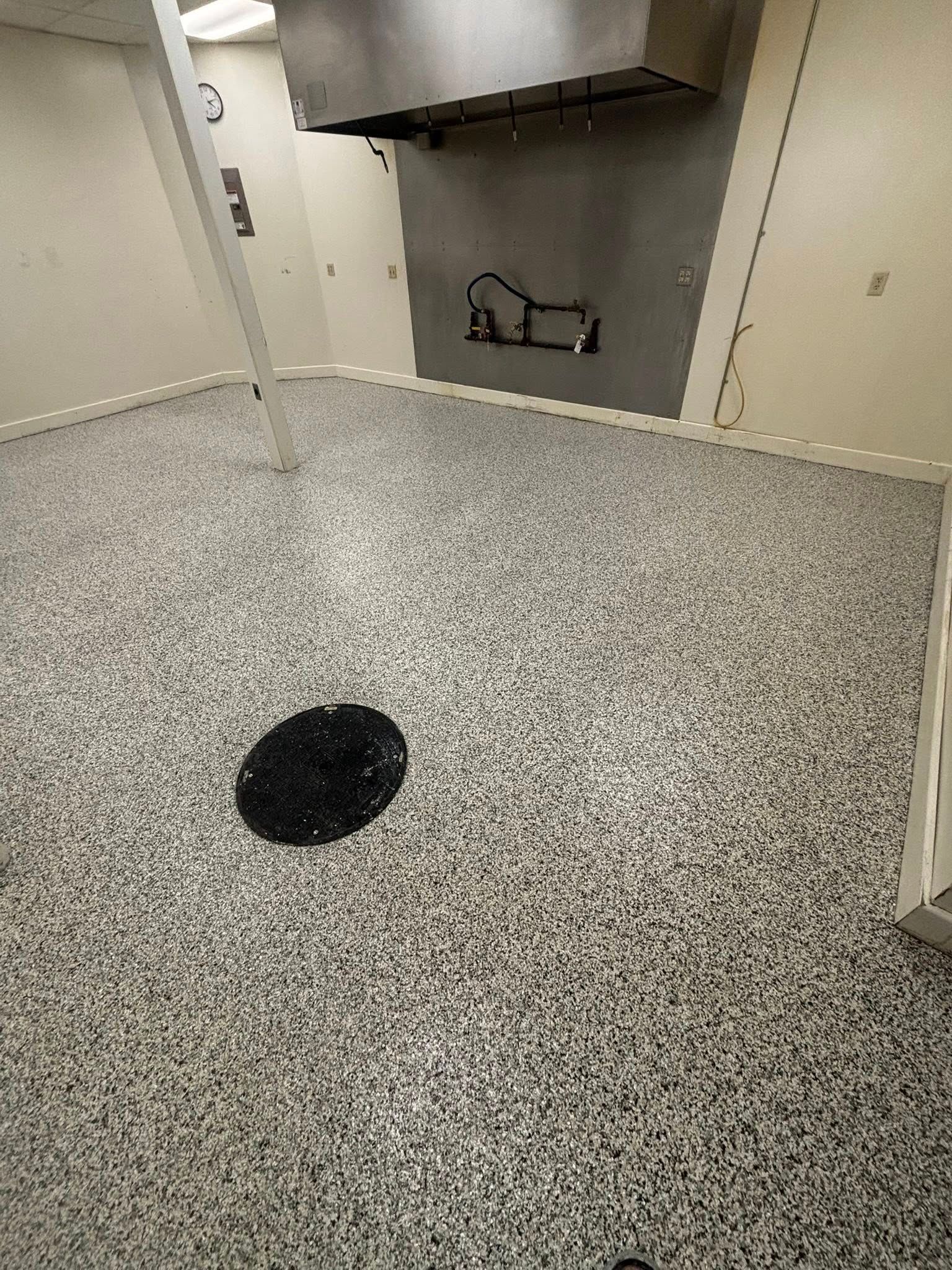 Gray speckled floor in a commercial kitchen area with a black floor drain and stainless steel equipment.