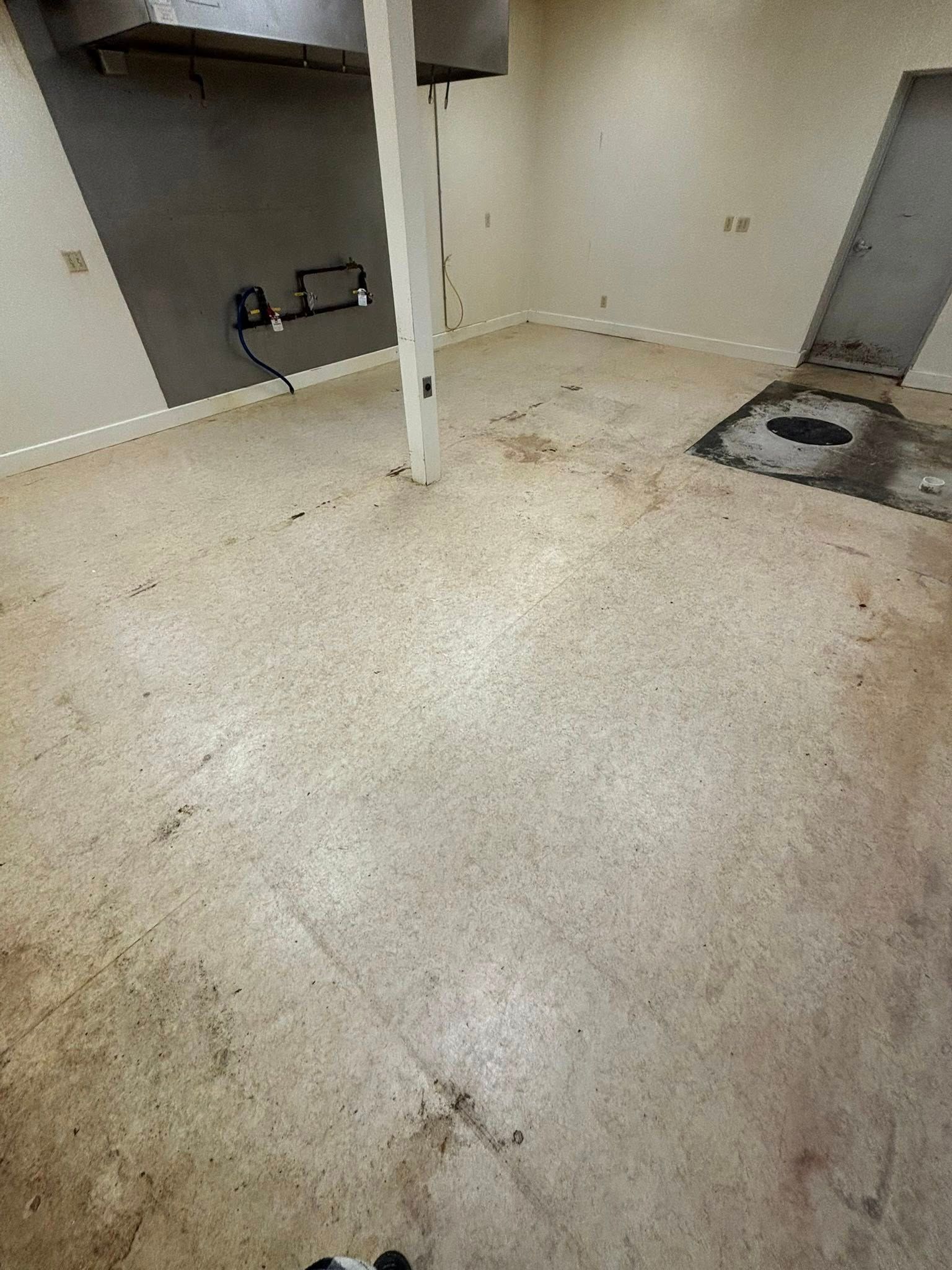 Empty unfinished room with concrete floor, exposed column, and wall fixtures near a drain area.