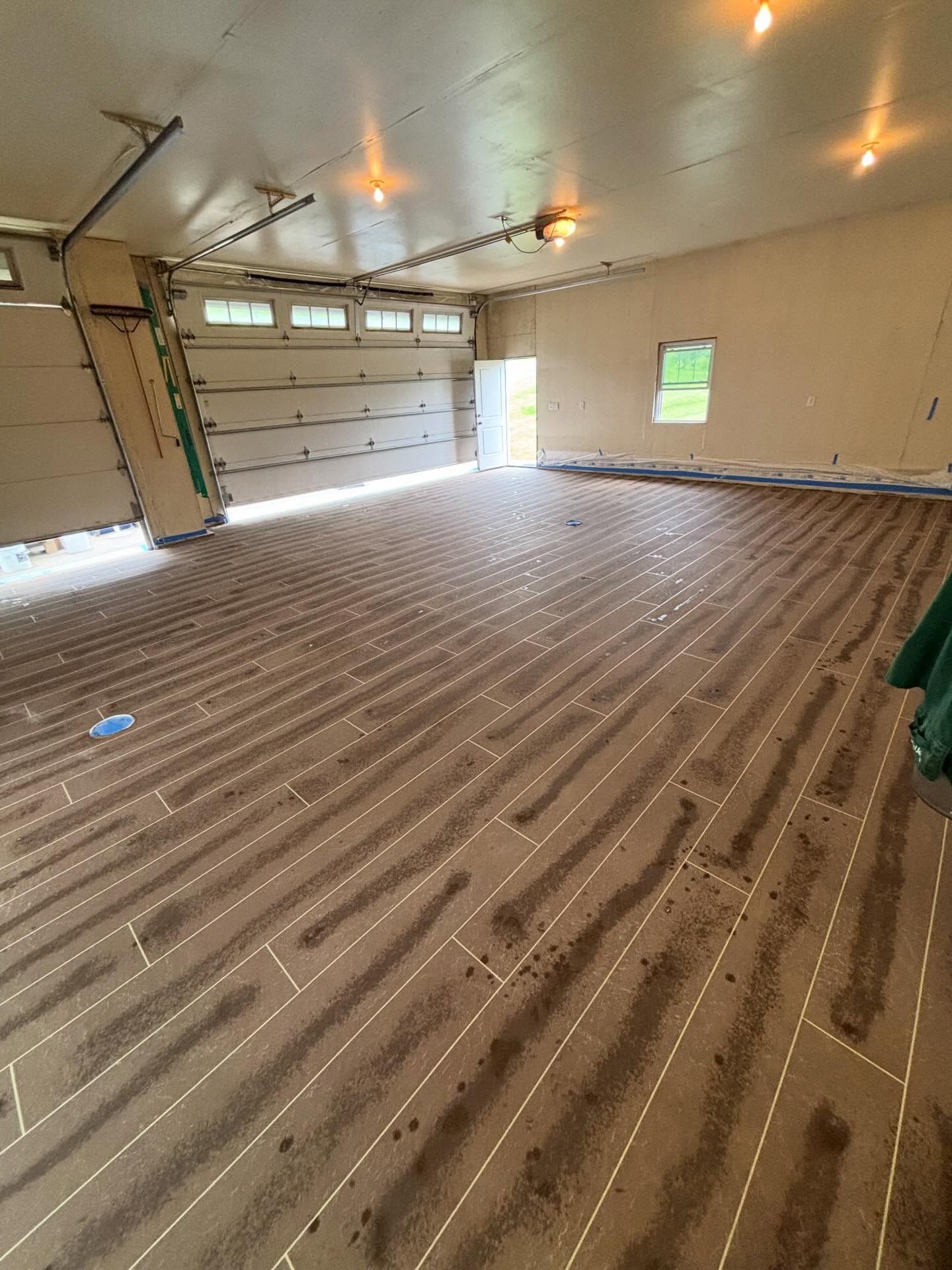 Empty unfinished garage with insulated floor, exposed ceiling lights, and a large garage door.
