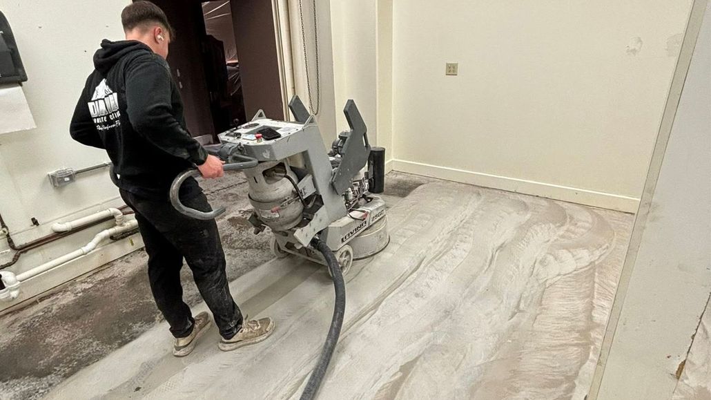 Worker operating floor grinder in a room with freshly sanded flooring and dust hose attached