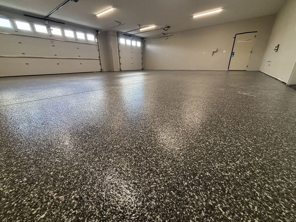 Empty garage with glossy speckled epoxy floor and closed white doors, viewed at a low angle.