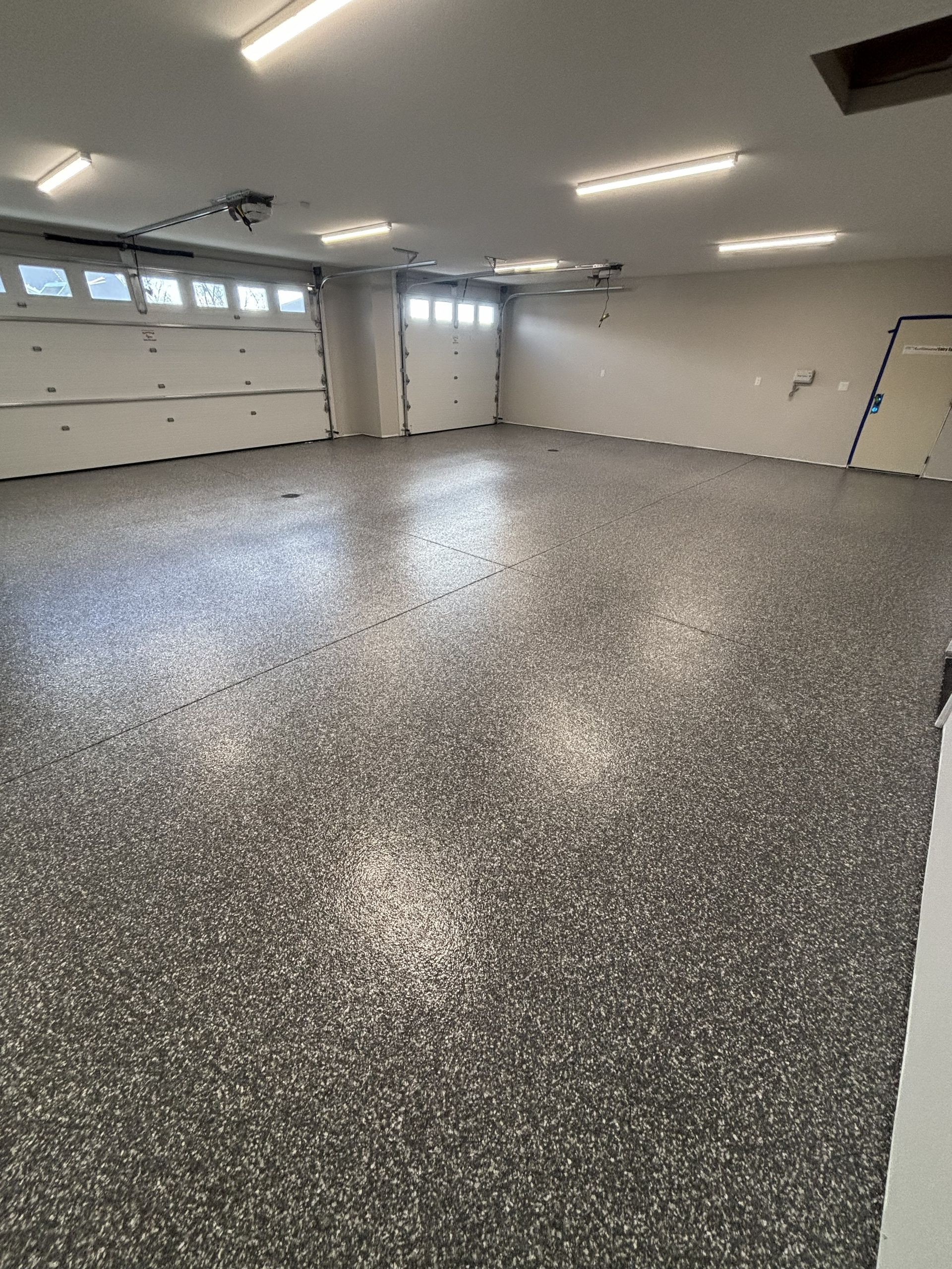Empty garage with speckled epoxy floor and overhead fluorescent lights
