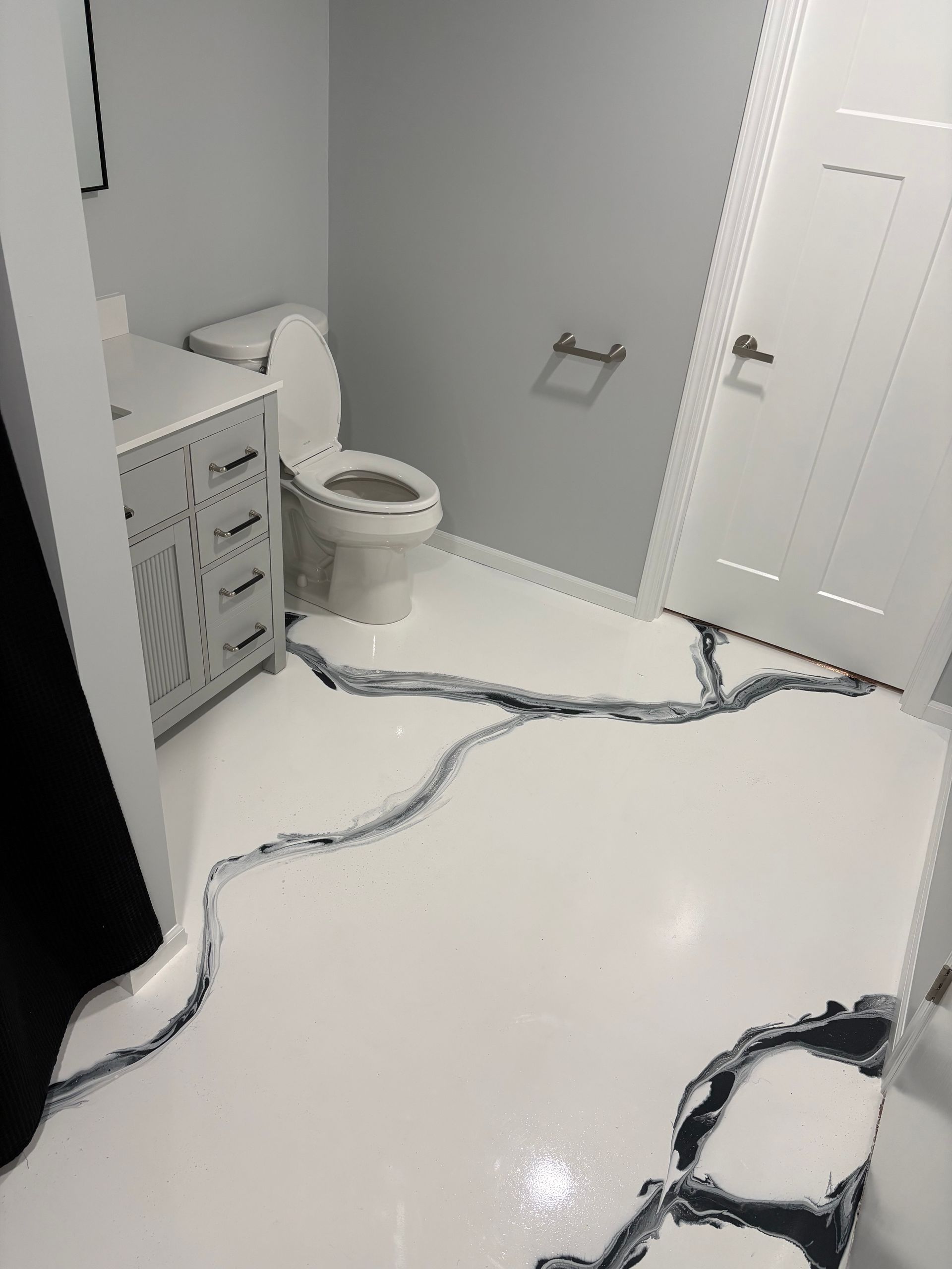 Small bathroom with toilet, vanity, and white floor partially covered by black-and-gray cords or hoses