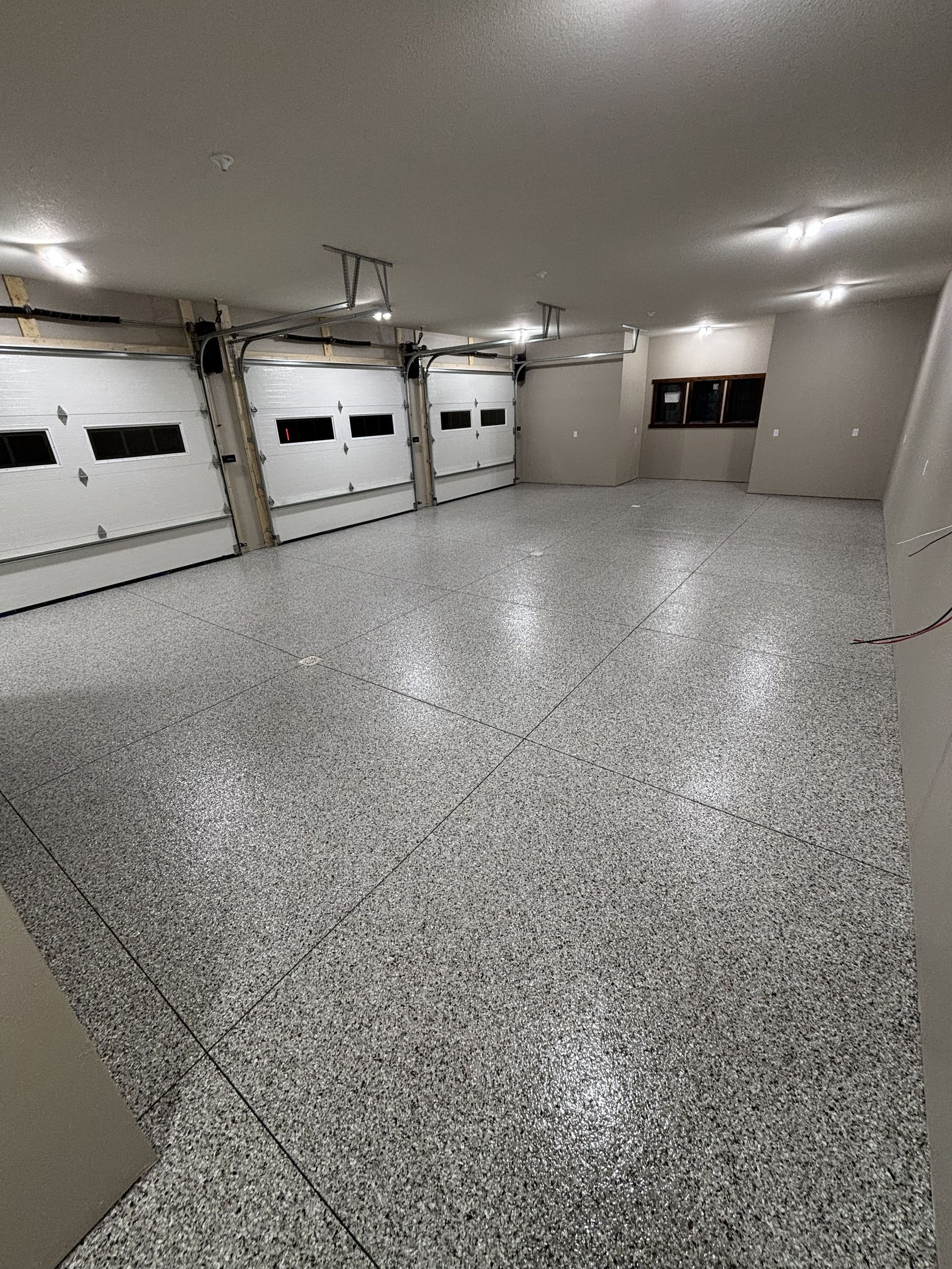 Empty residential garage with speckled epoxy floor and white walls, lit by ceiling lights