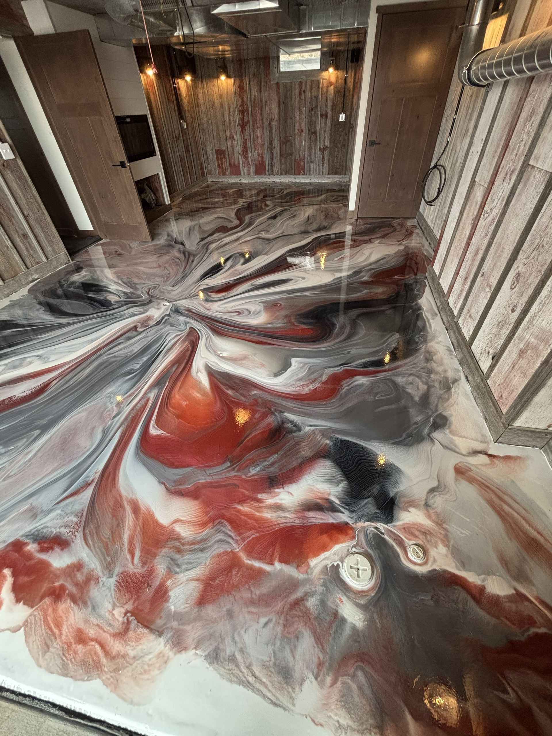 Swirling red, white, and black marbled floor in a modern hallway with warm wall lights
