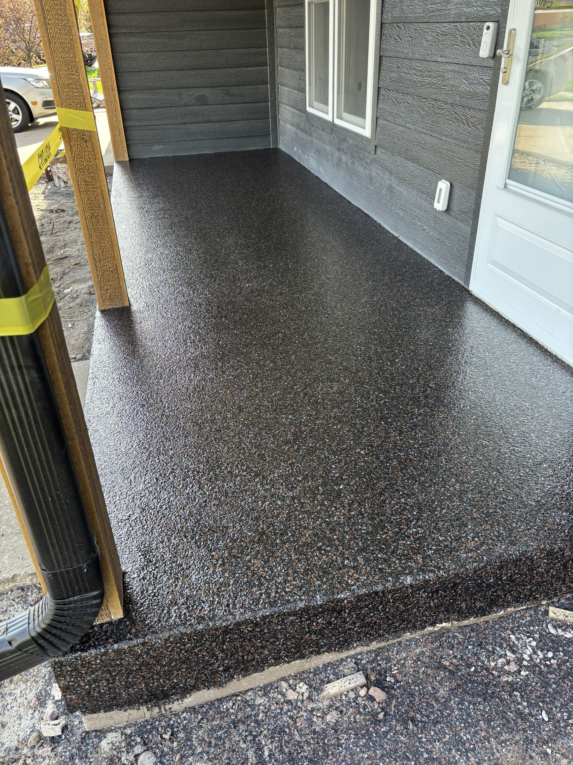 Front porch with dark speckled flooring, gray wall, white door, and yellow post railing.