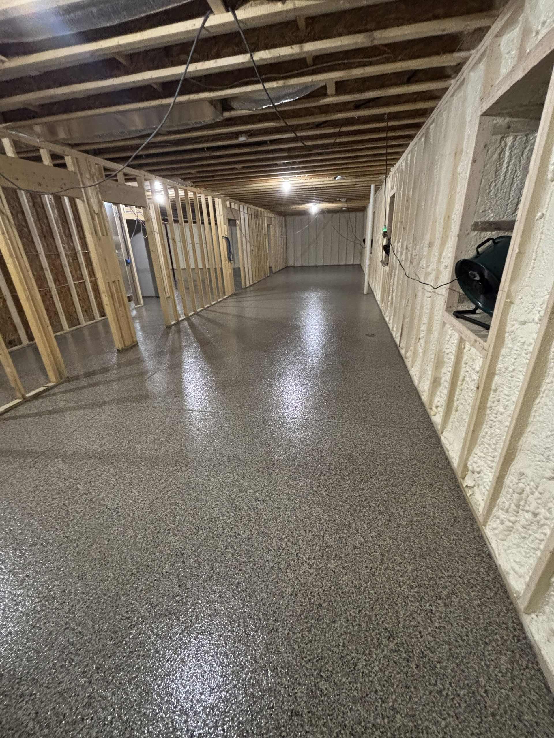 Unfinished basement with a newly poured speckled concrete floor and exposed wooden framing.