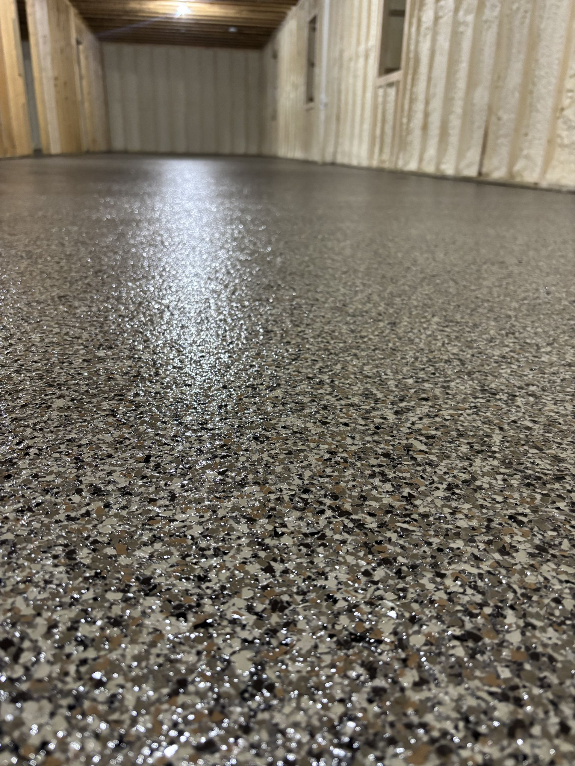Shiny speckled epoxy floor in a narrow hallway or storage corridor with wood-paneled walls