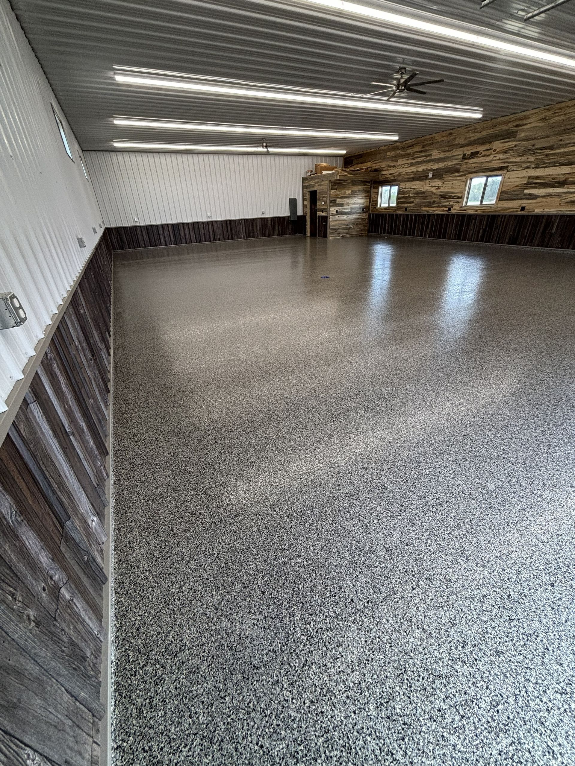 Empty indoor room with speckled floor, fluorescent lights, and stone wall accents