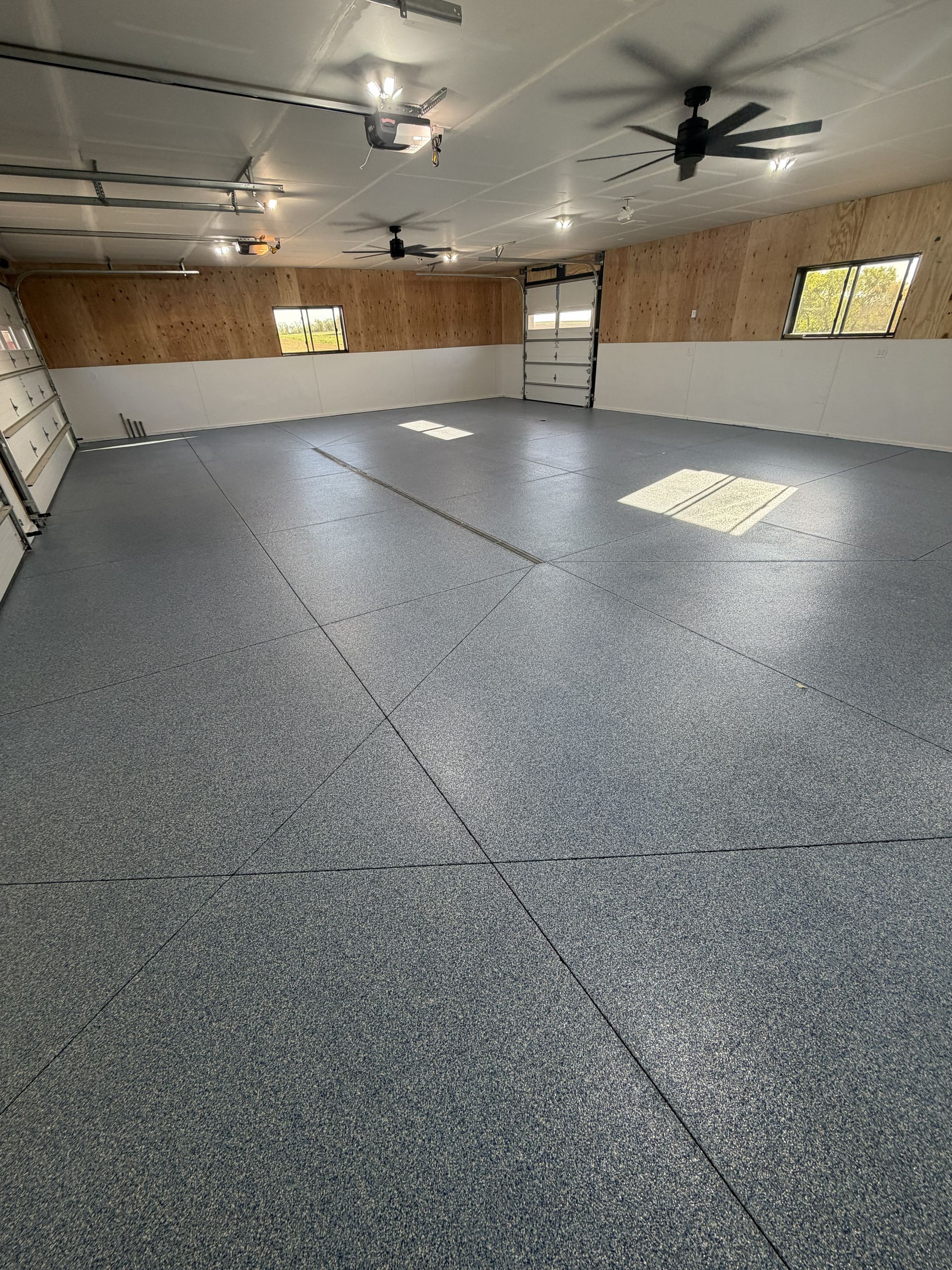 Empty speckled garage with ceiling fans, overhead lights, and windows along one wall