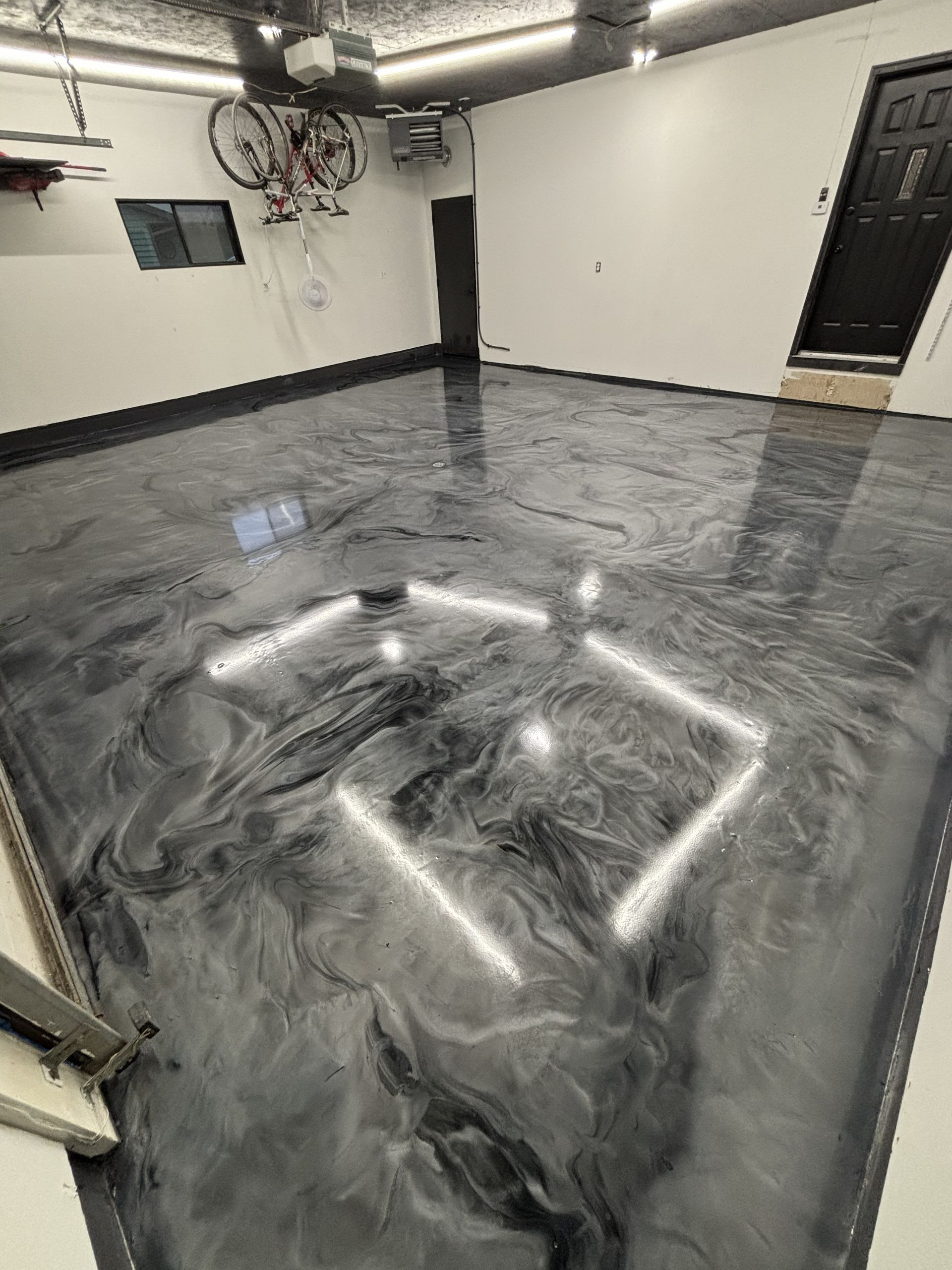 Shiny gray epoxy floor in a garage or basement with white walls and a black door.