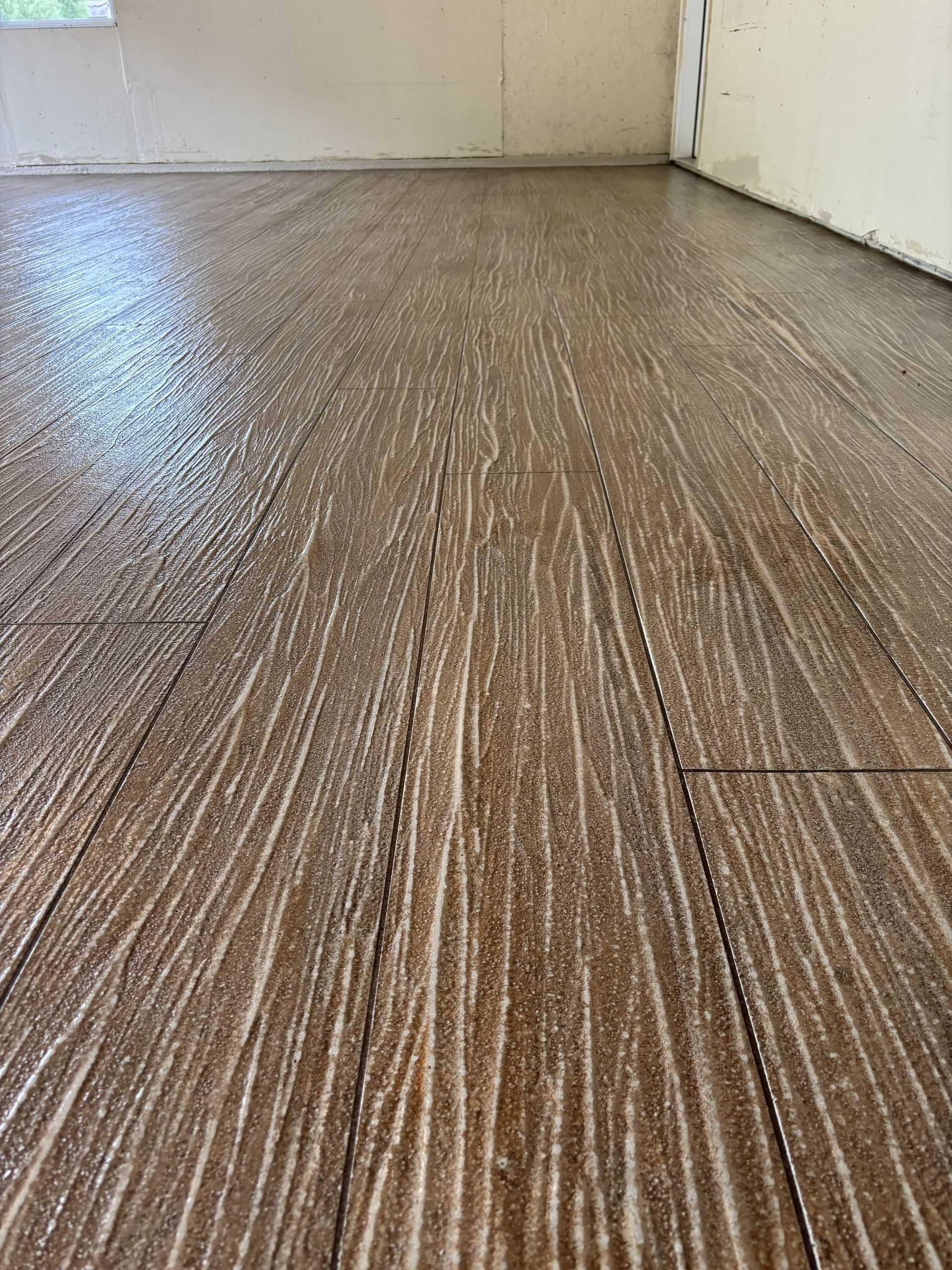 Close-up of a wet, textured wood-pattern floor near a wall and doorway.