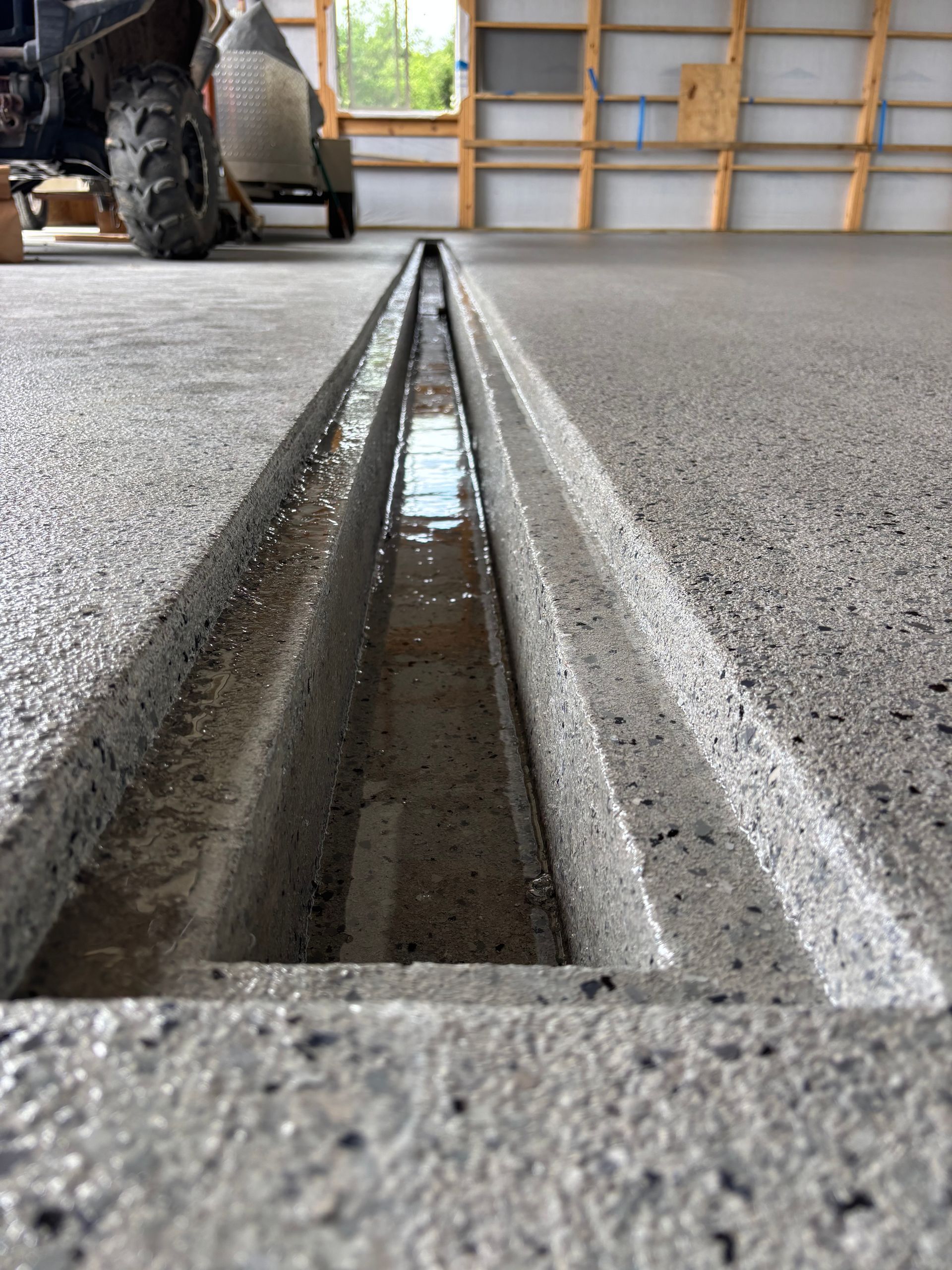 Concrete floor expansion joint trench in a garage, with a forklift blurred in the background.