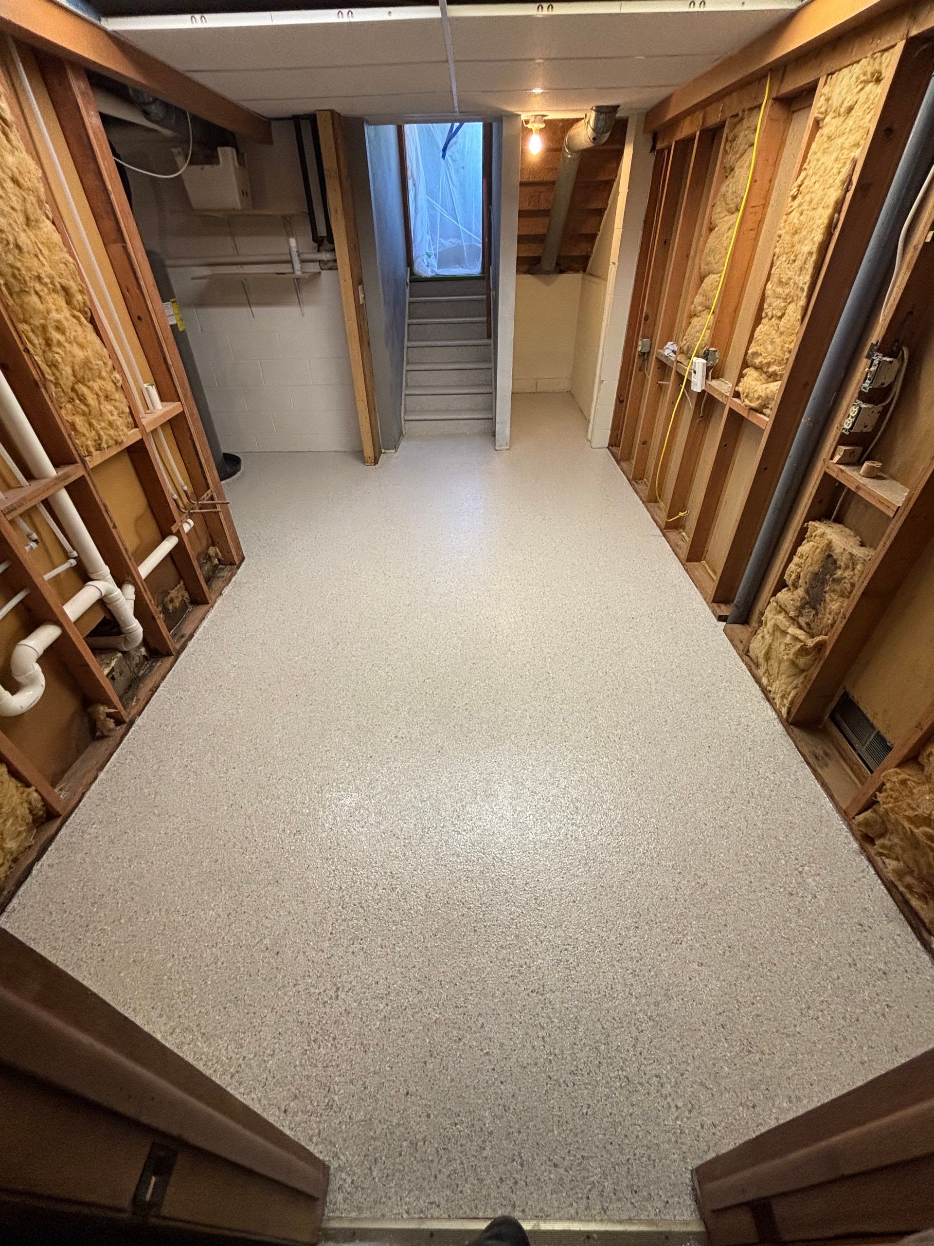 Basement stairwell landing with unfinished wooden walls, framed by open storage on both sides.