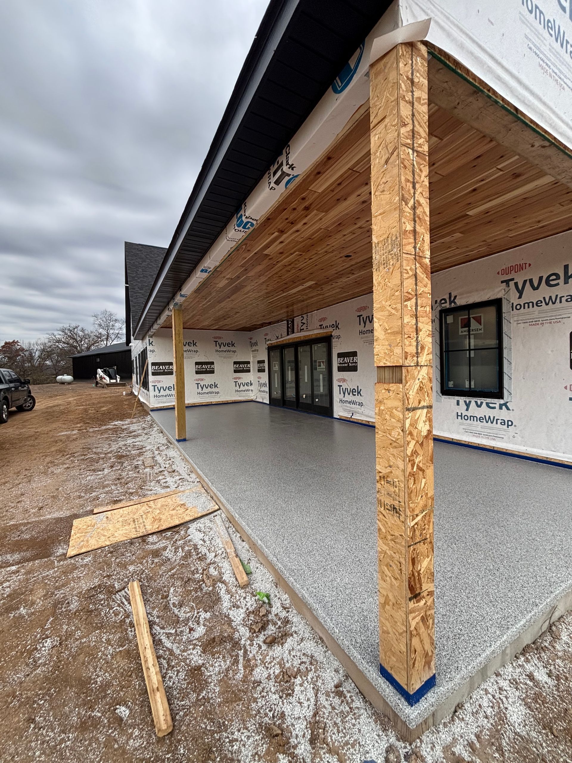 Partially built storefront with exposed wood framing, gray gravel walkway, and cloudy sky