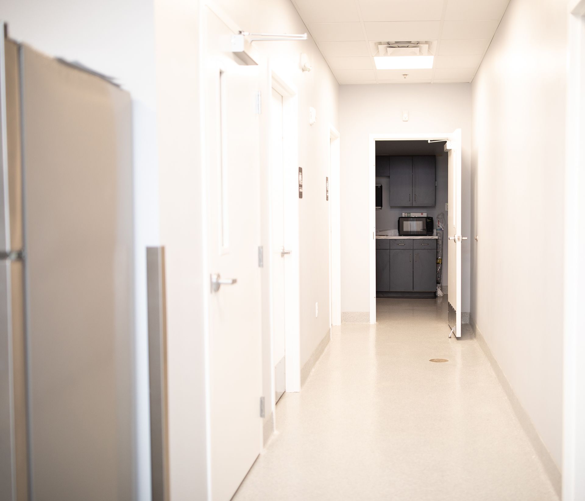 A long hallway at Bowling Green Veterinary Emergency Clinic with a refrigerator and a kitchen in the background.