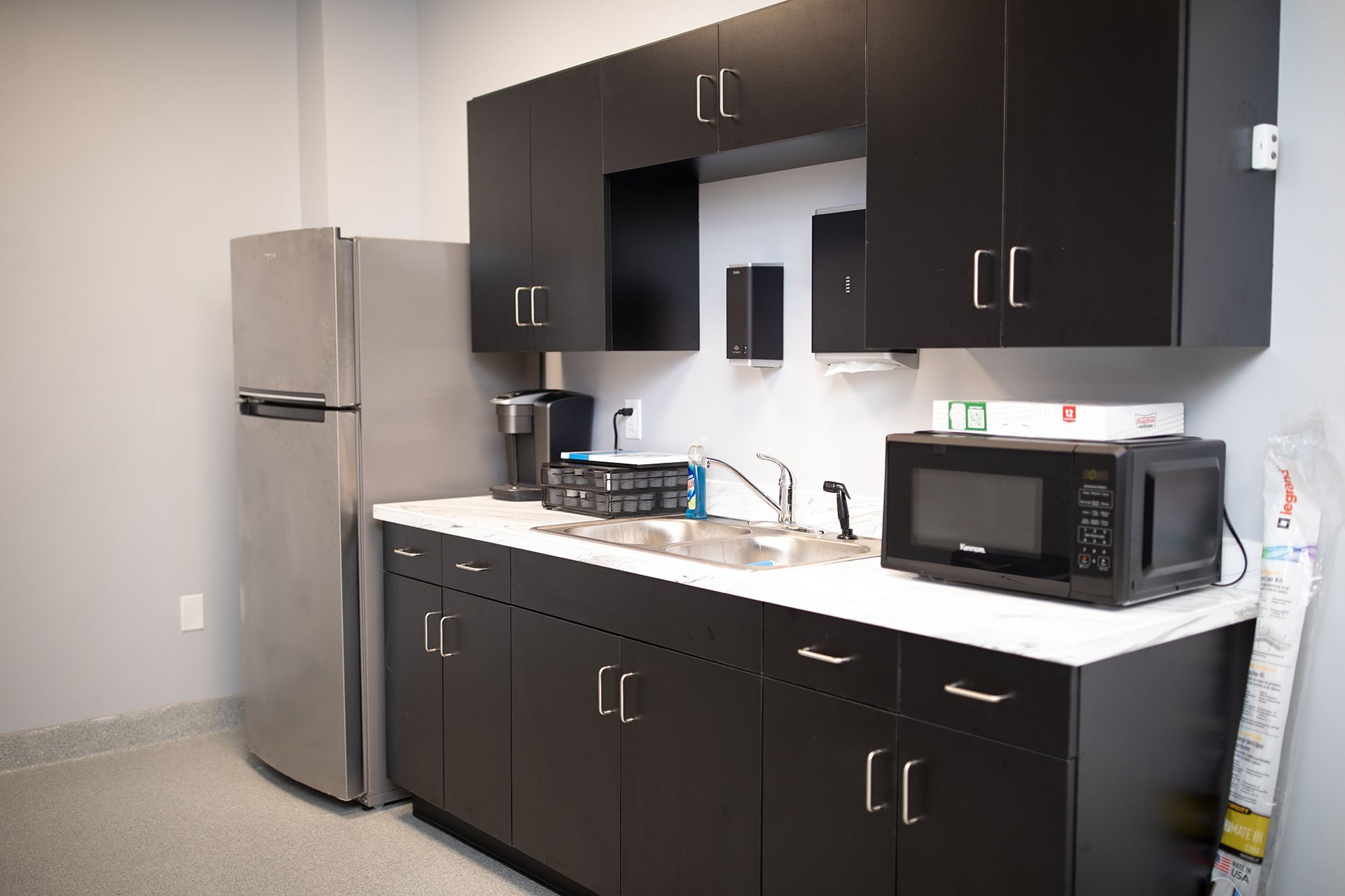 A kitchen with black cabinets and a stainless steel refrigerator.