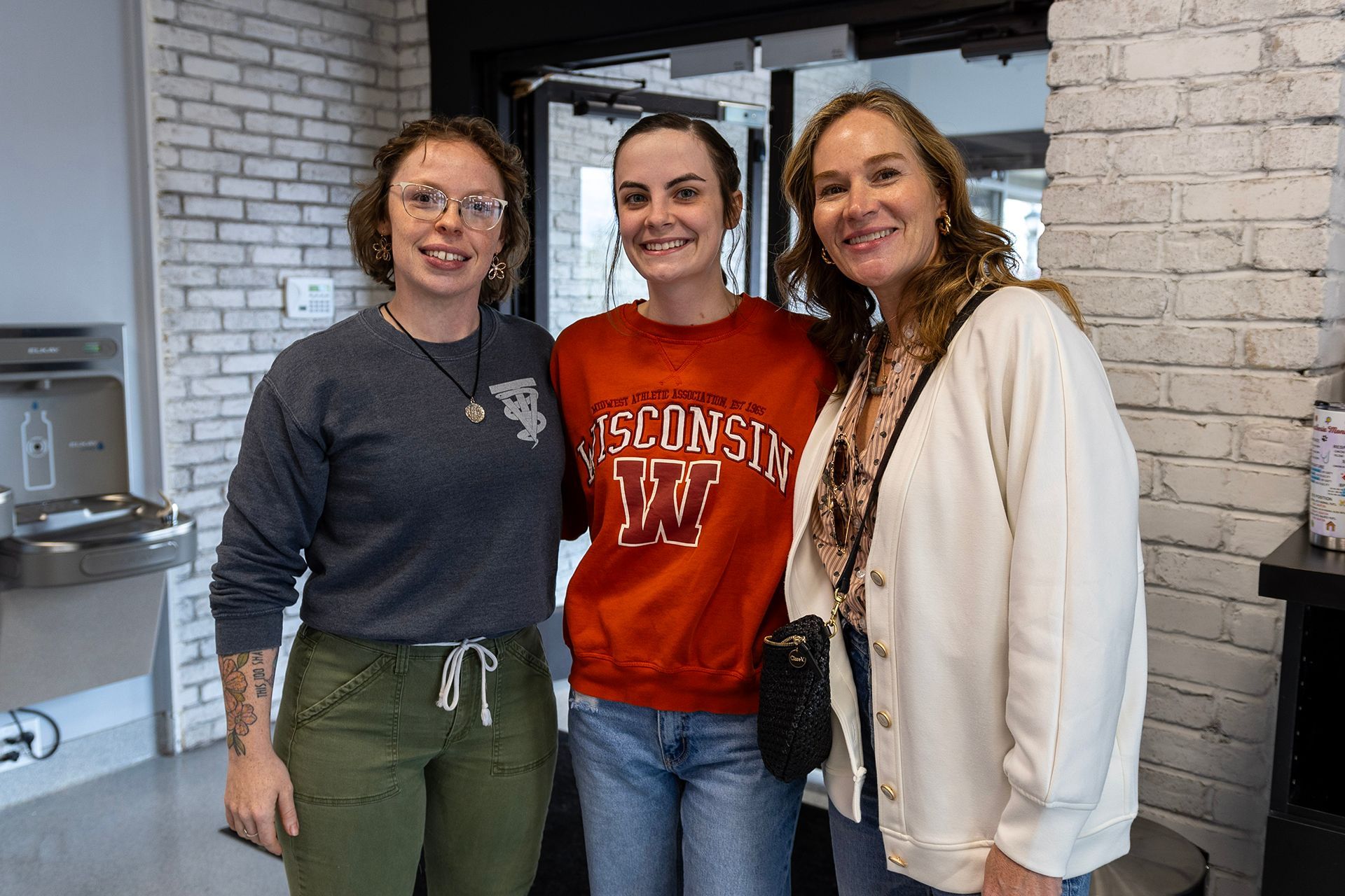 Three women are posing for a picture in front of a brick wall at Bowling Green Veterinary Emergency Clinic.