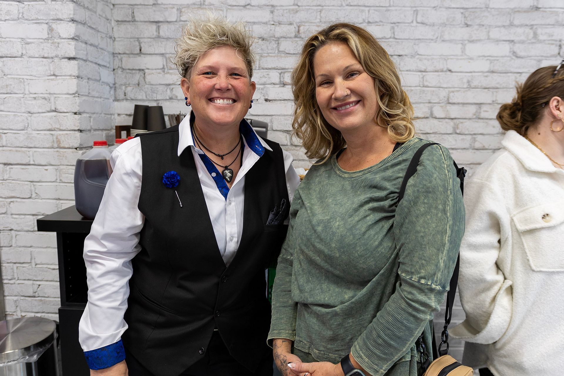 Two women are posing for a picture in front of a white brick wall.
