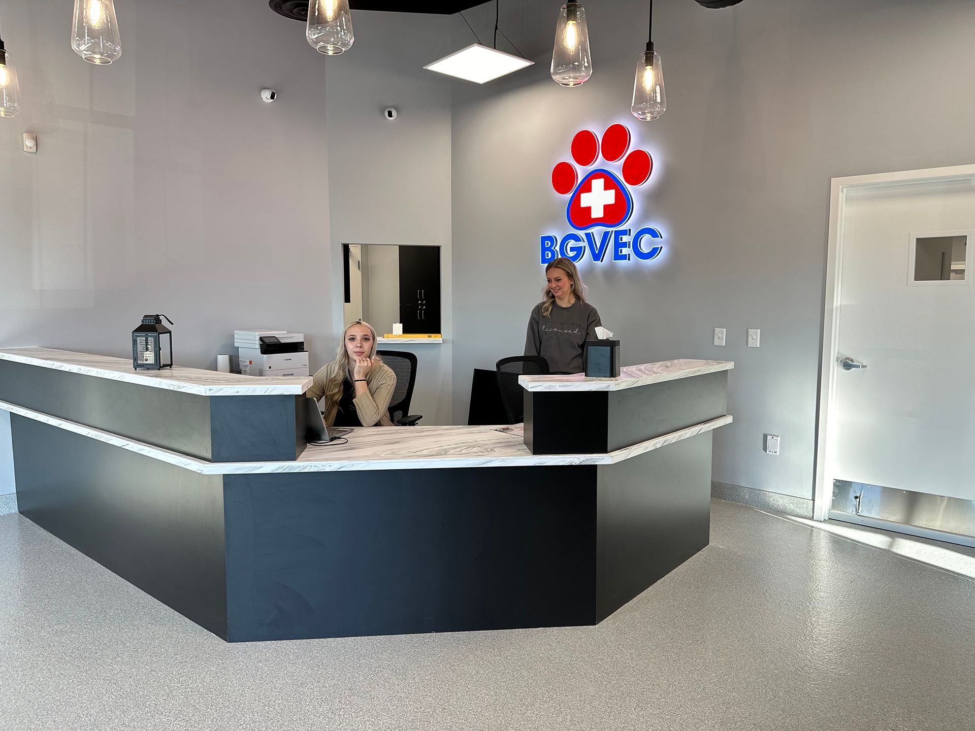 Two women at Bowling Green Veterinary Emergency Clinic are standing at a reception desk in a veterinary clinic.