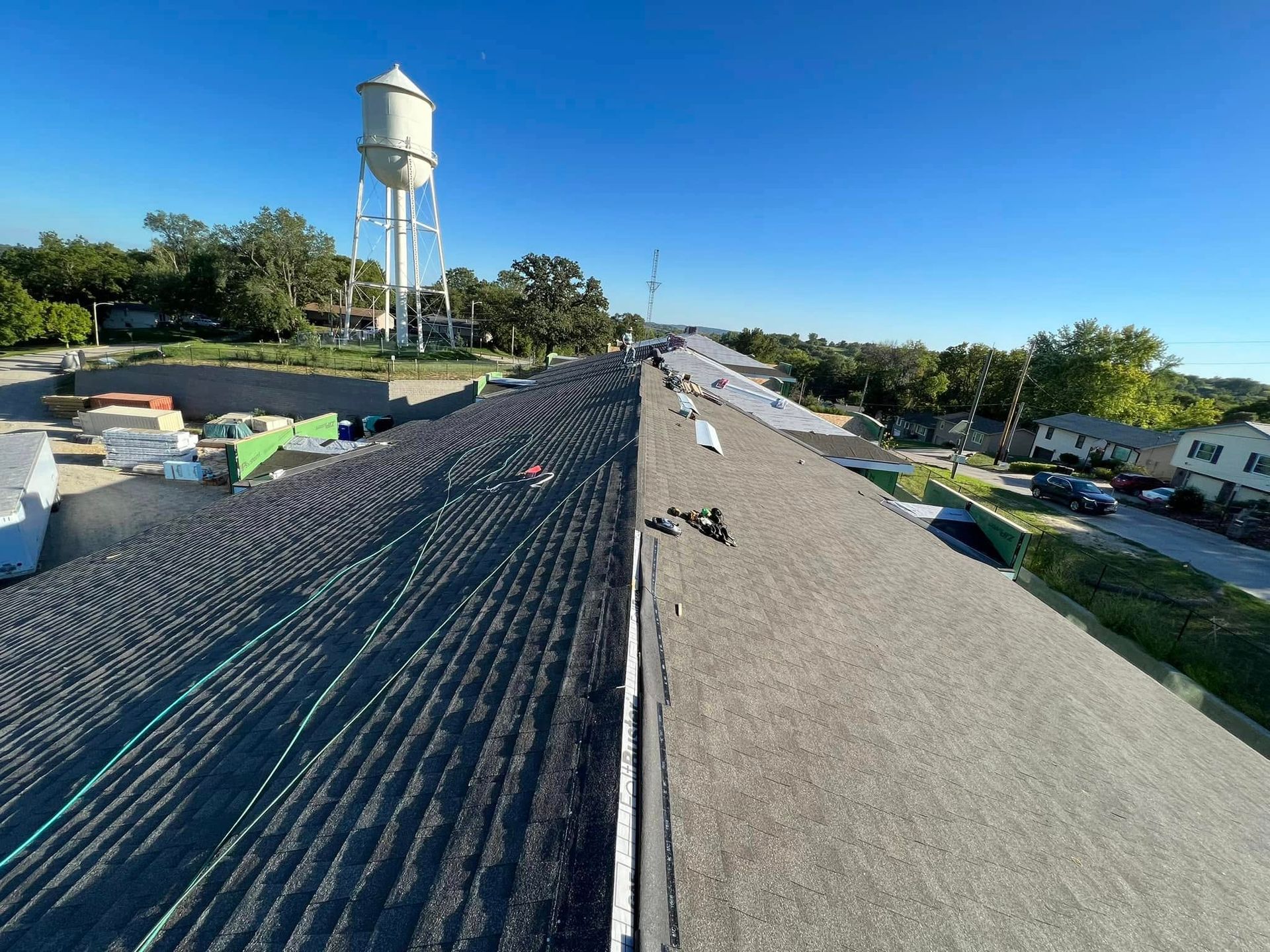 Rooftop under construction with workers, gravel surface, and a water tower against a clear blue sky.
