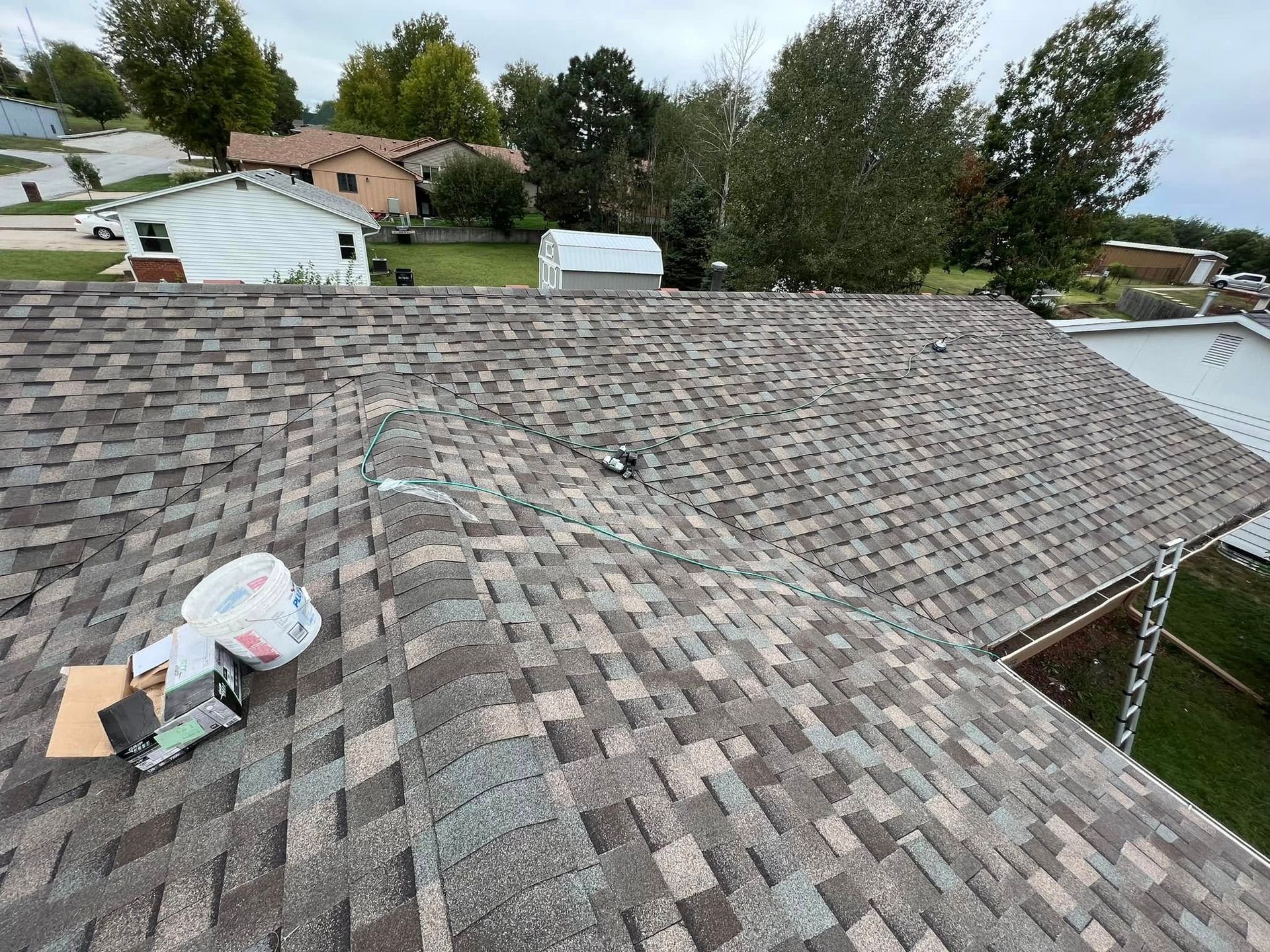 Roofer working on a gray shingle roof with tools and materials near the ridge