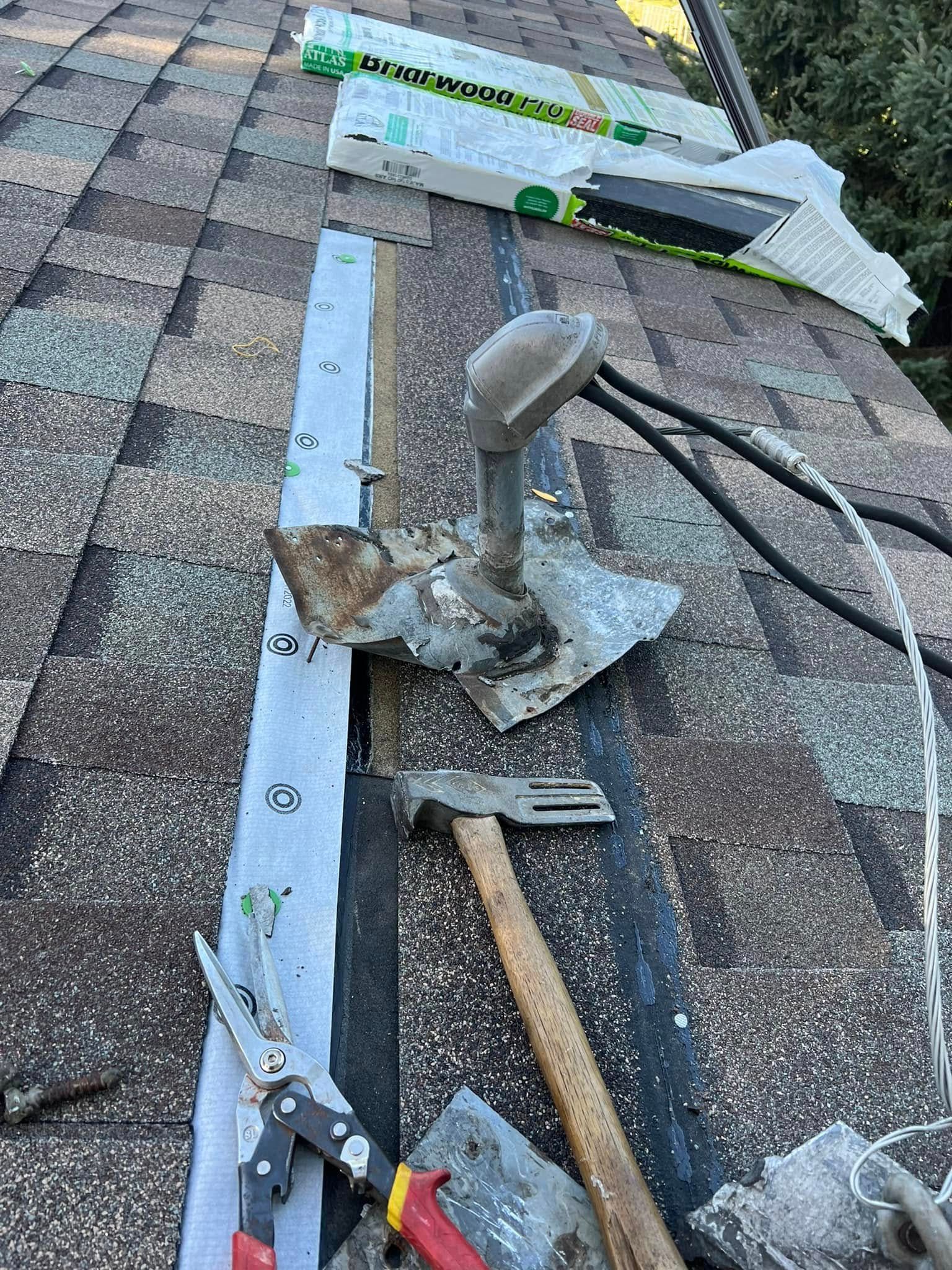Roof repair tools and materials scattered on a shingled roof near a vent pipe and taped flashing.