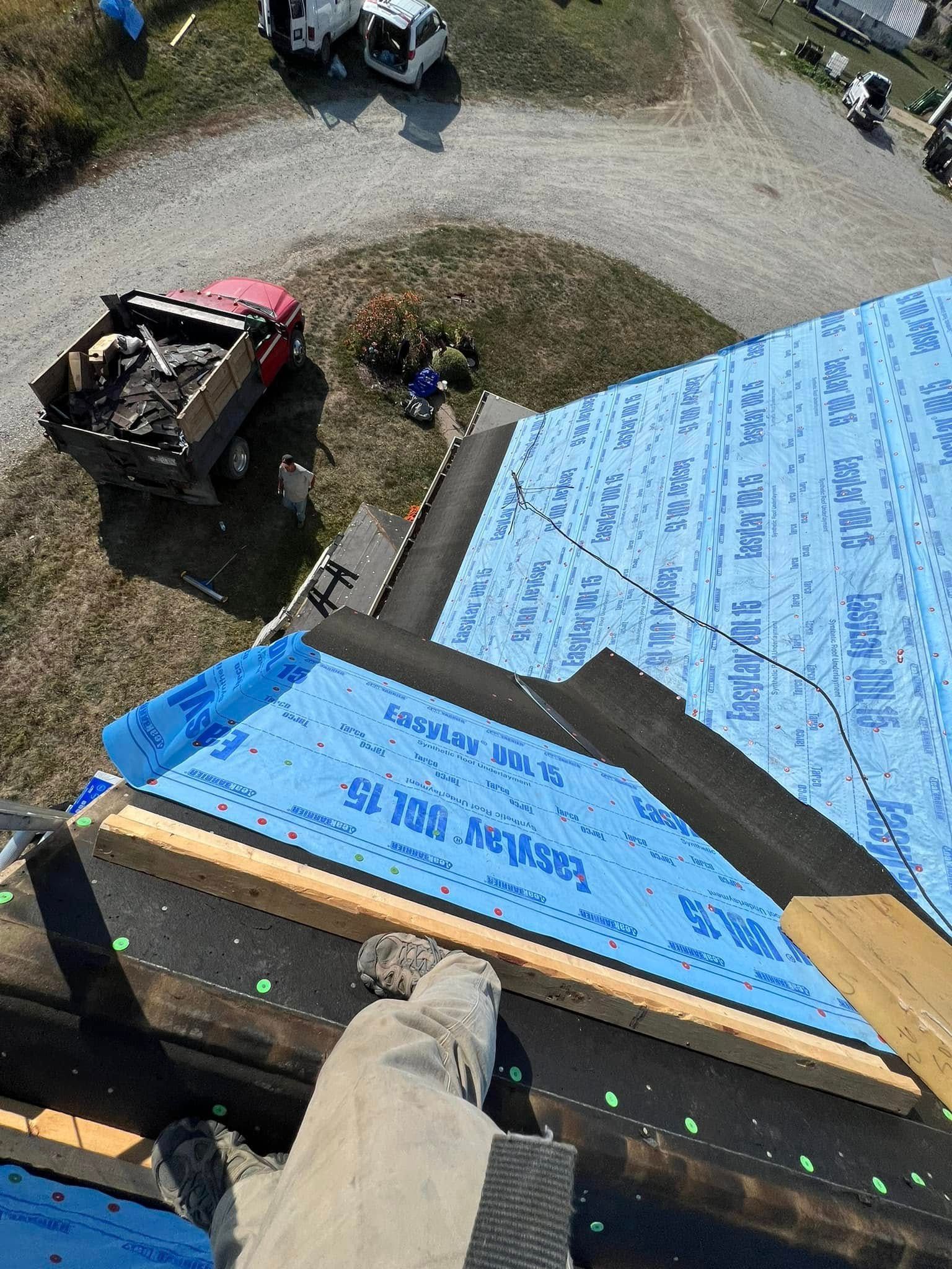 Roofer’s view of blue tar paper on a roof, with workers and trucks below