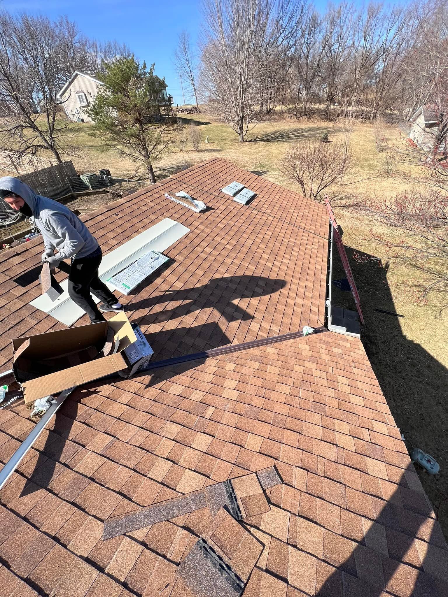 Worker repairing a brown shingle roof with replacement materials on a sunny day