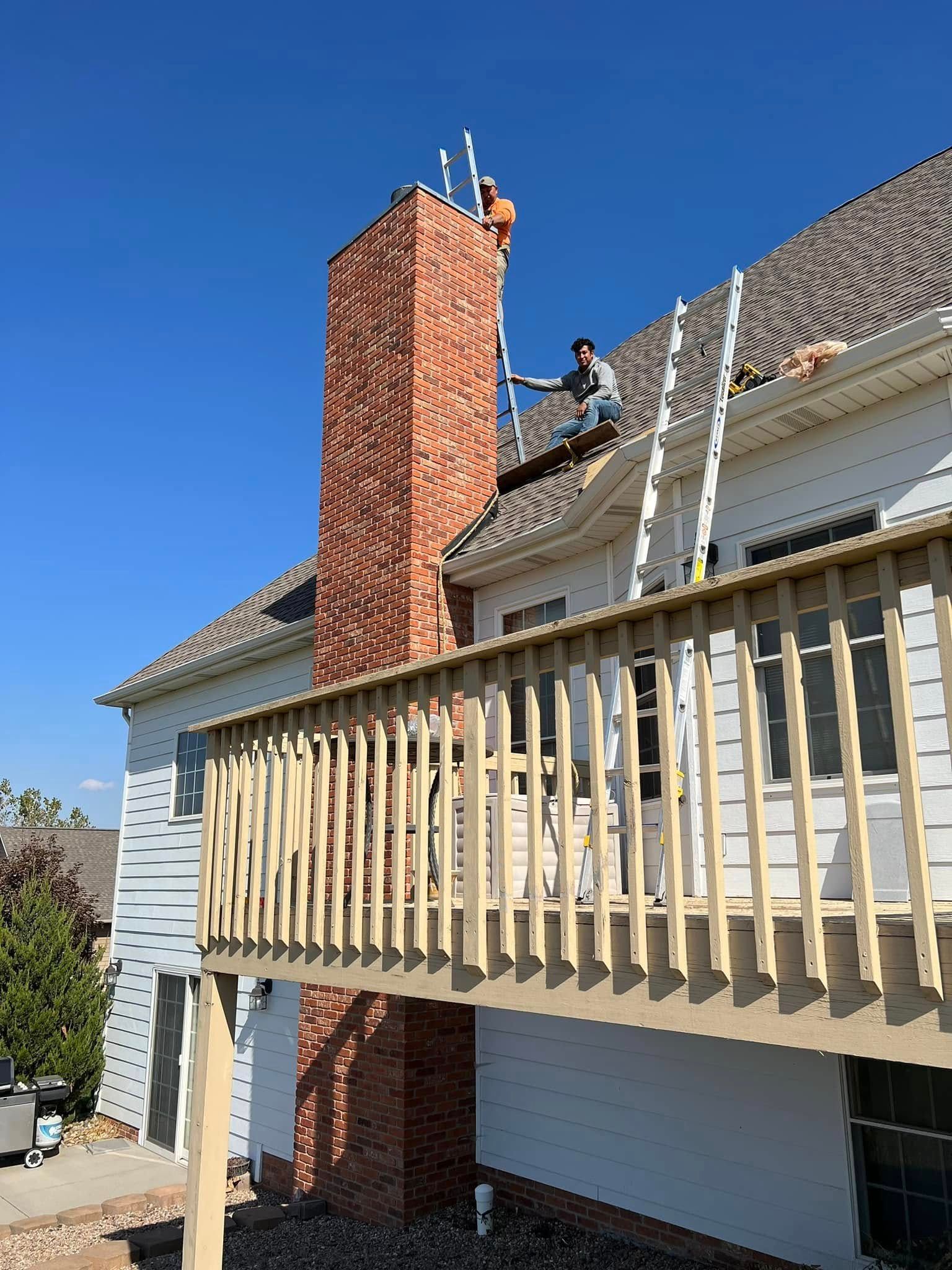 House under construction with a worker on a roof, chimney brickwork, and a partially built wooden balcony.
