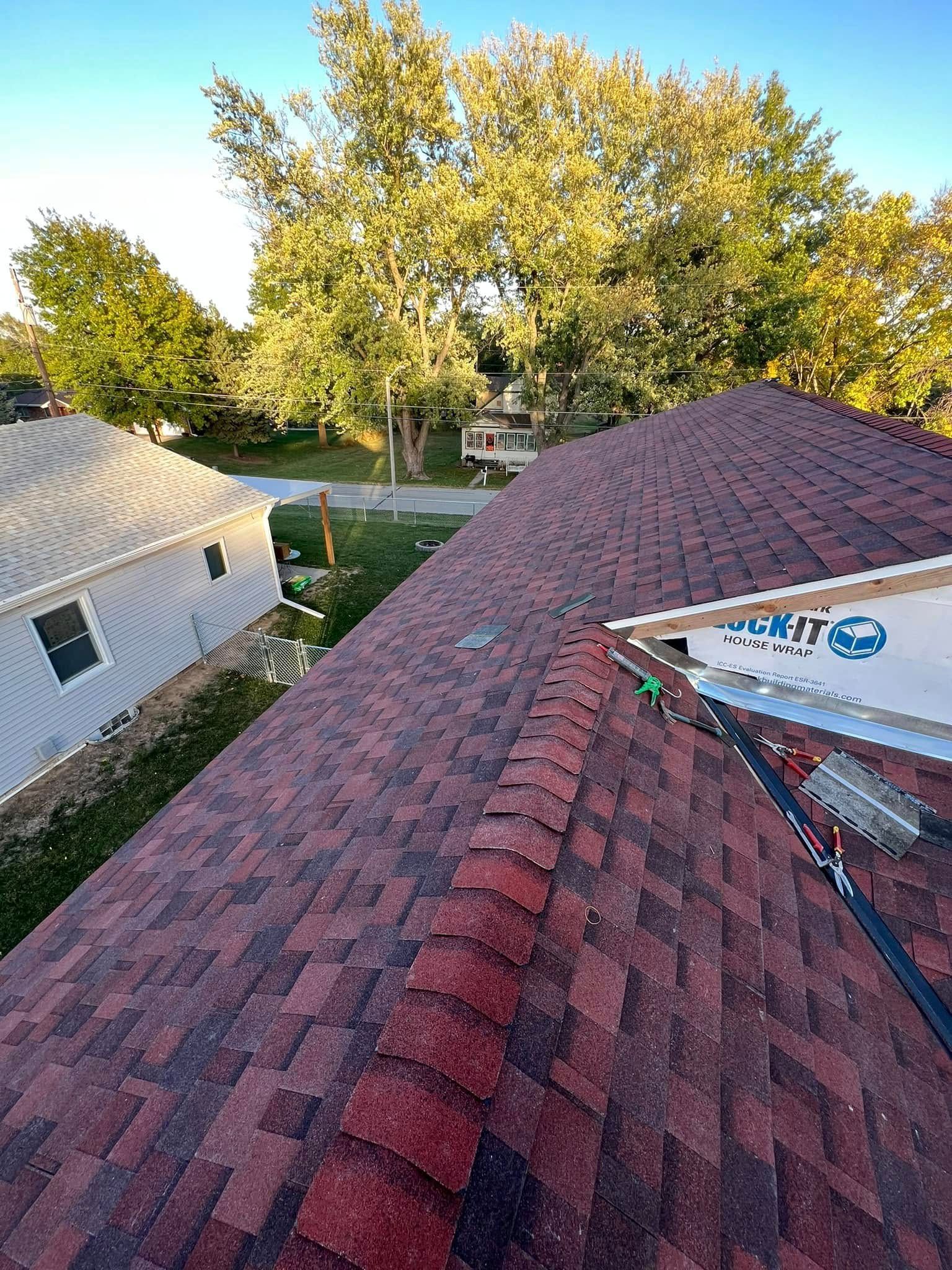 Rooftop view of red shingles, a house, and trees in warm evening light