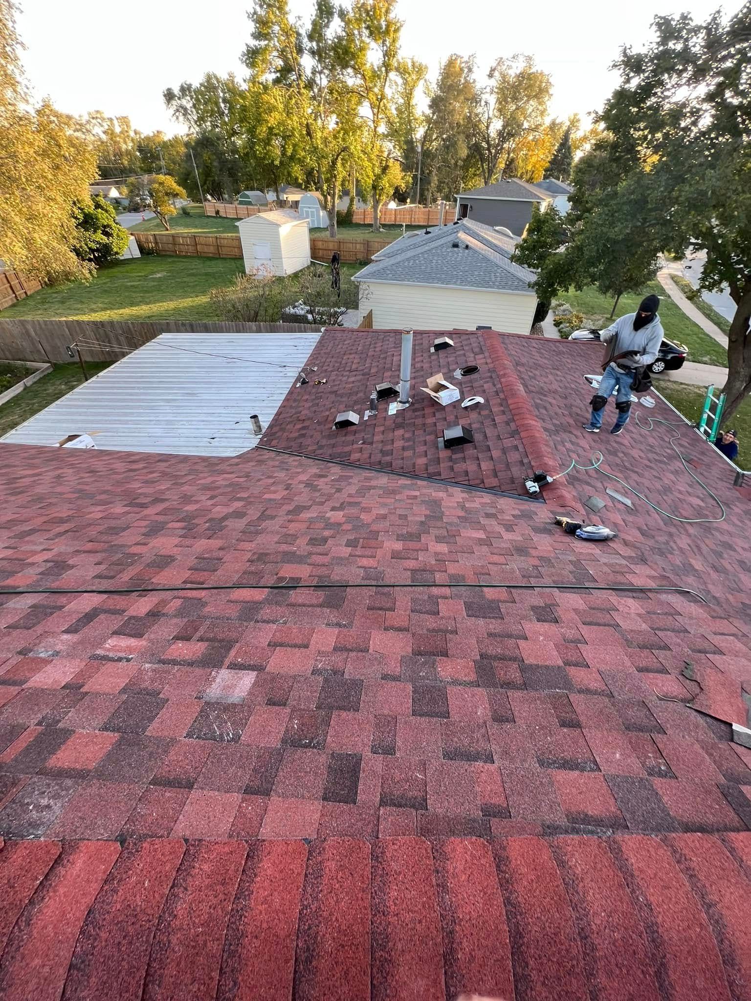 Roofers working on a red shingle roof with tools and materials at sunset